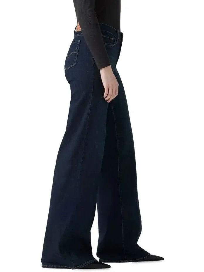 Side view of dark wide-leg denim jeans paired with a black fitted long-sleeve top and pointed shoes