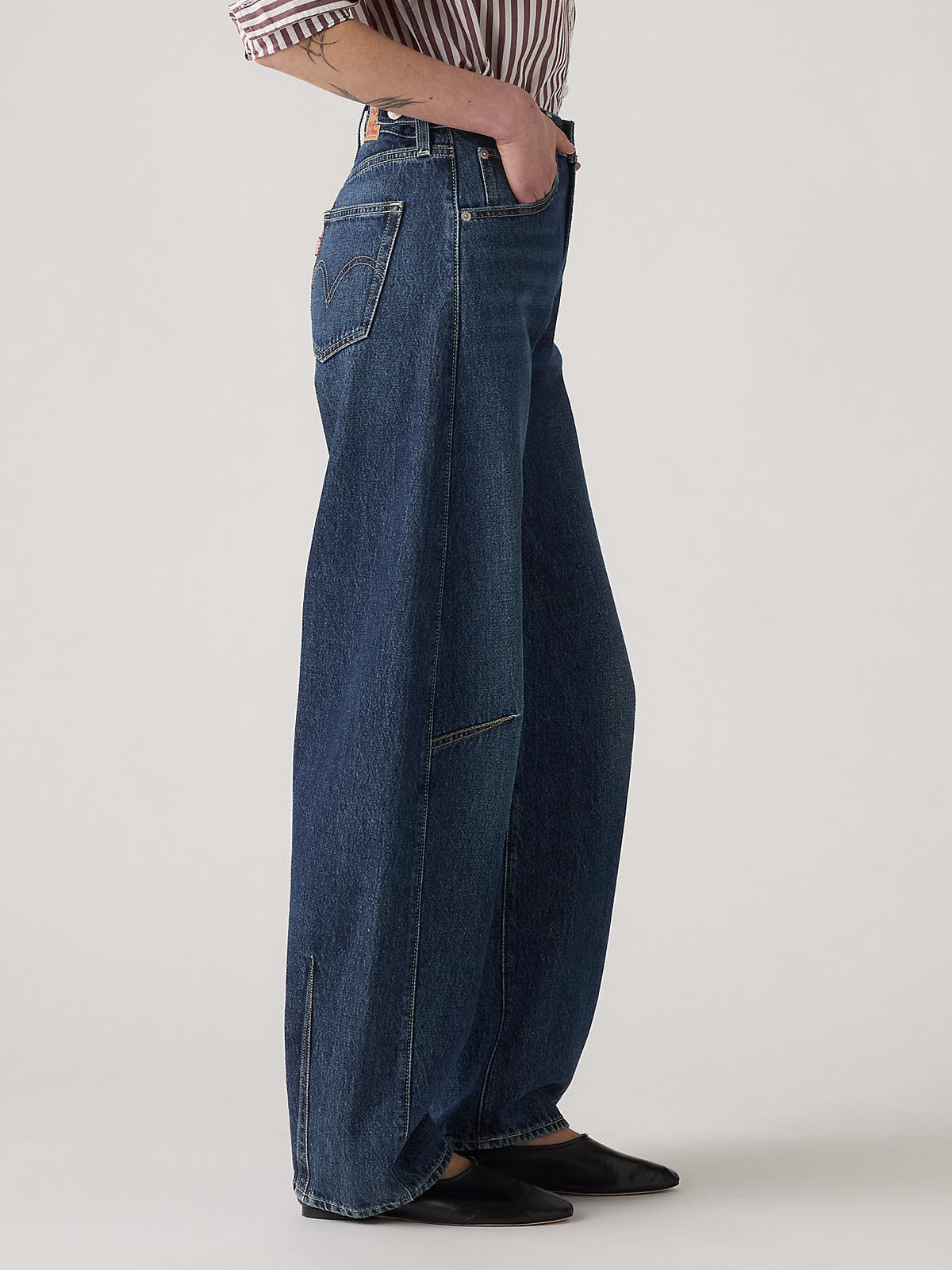 Side view of wide-leg dark denim jeans paired with a striped shirt and black pointed shoes.