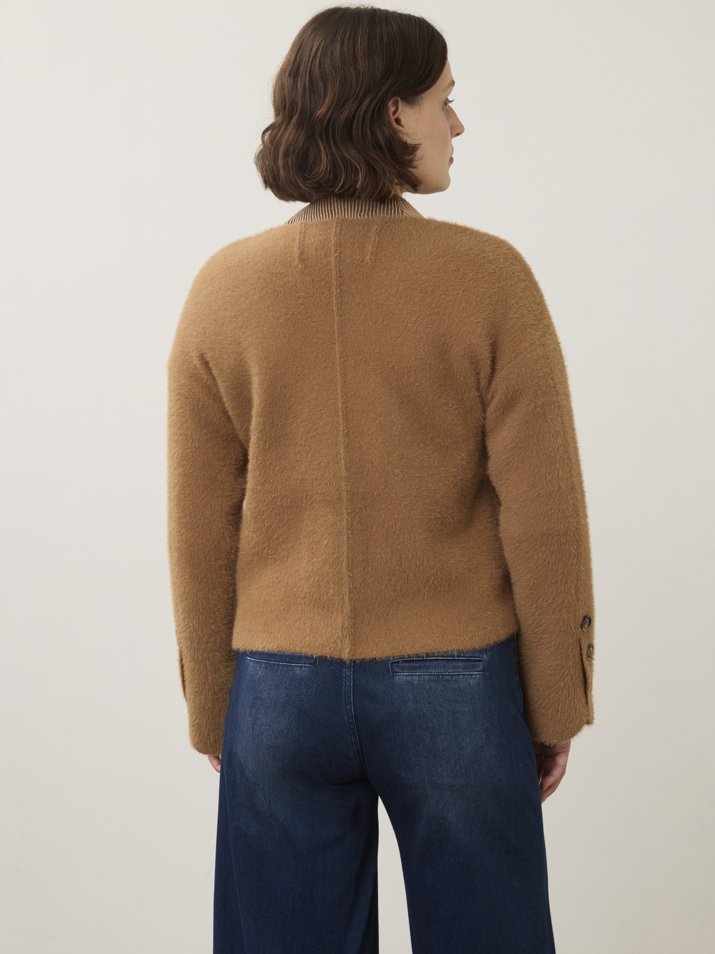 Back view of a camel-colored fuzzy sweater paired with dark blue loose-fitting denim pants.
