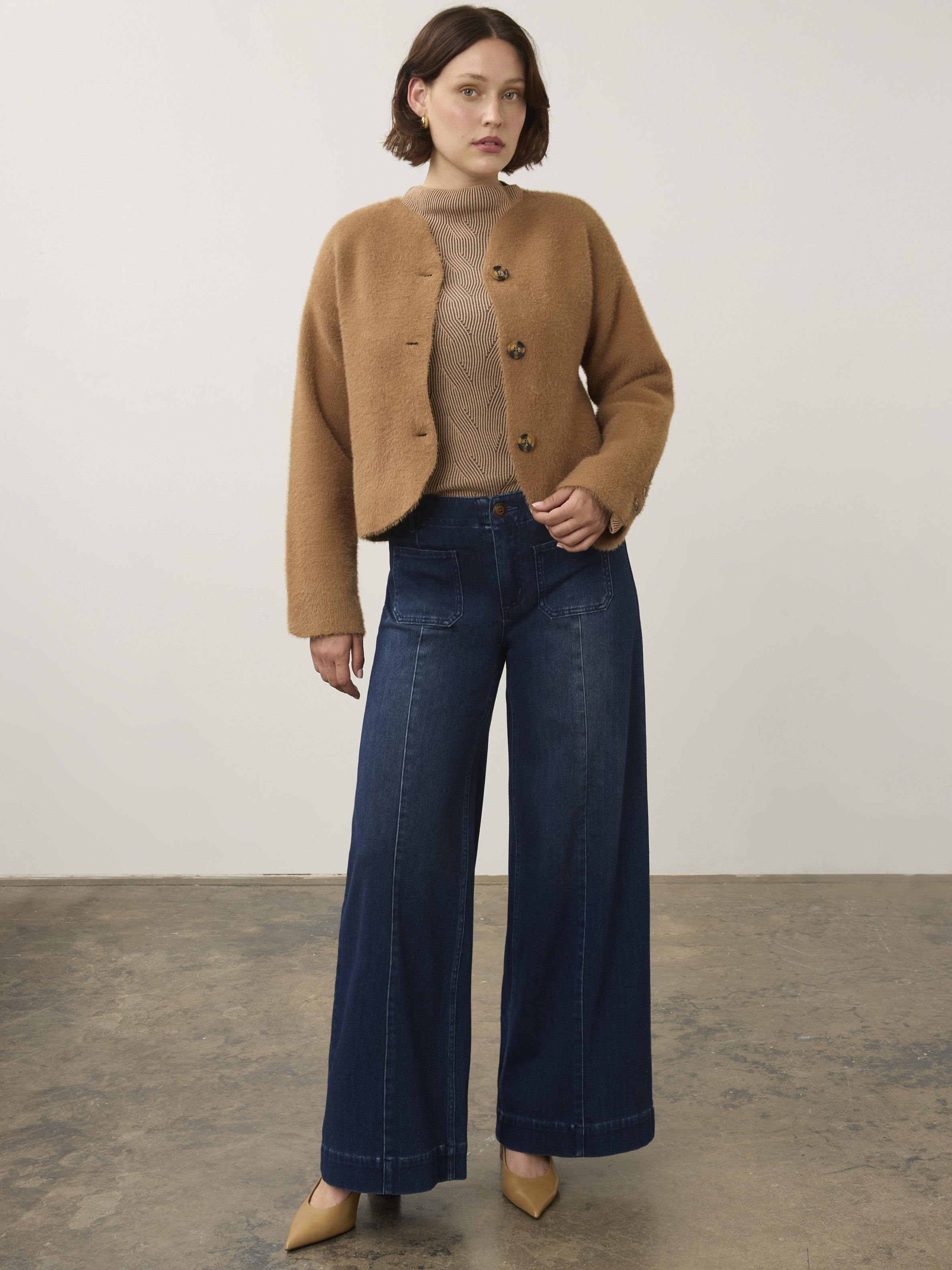 Camel-colored button-up fuzzy jacket paired with a brown knit top and wide-leg dark denim jeans