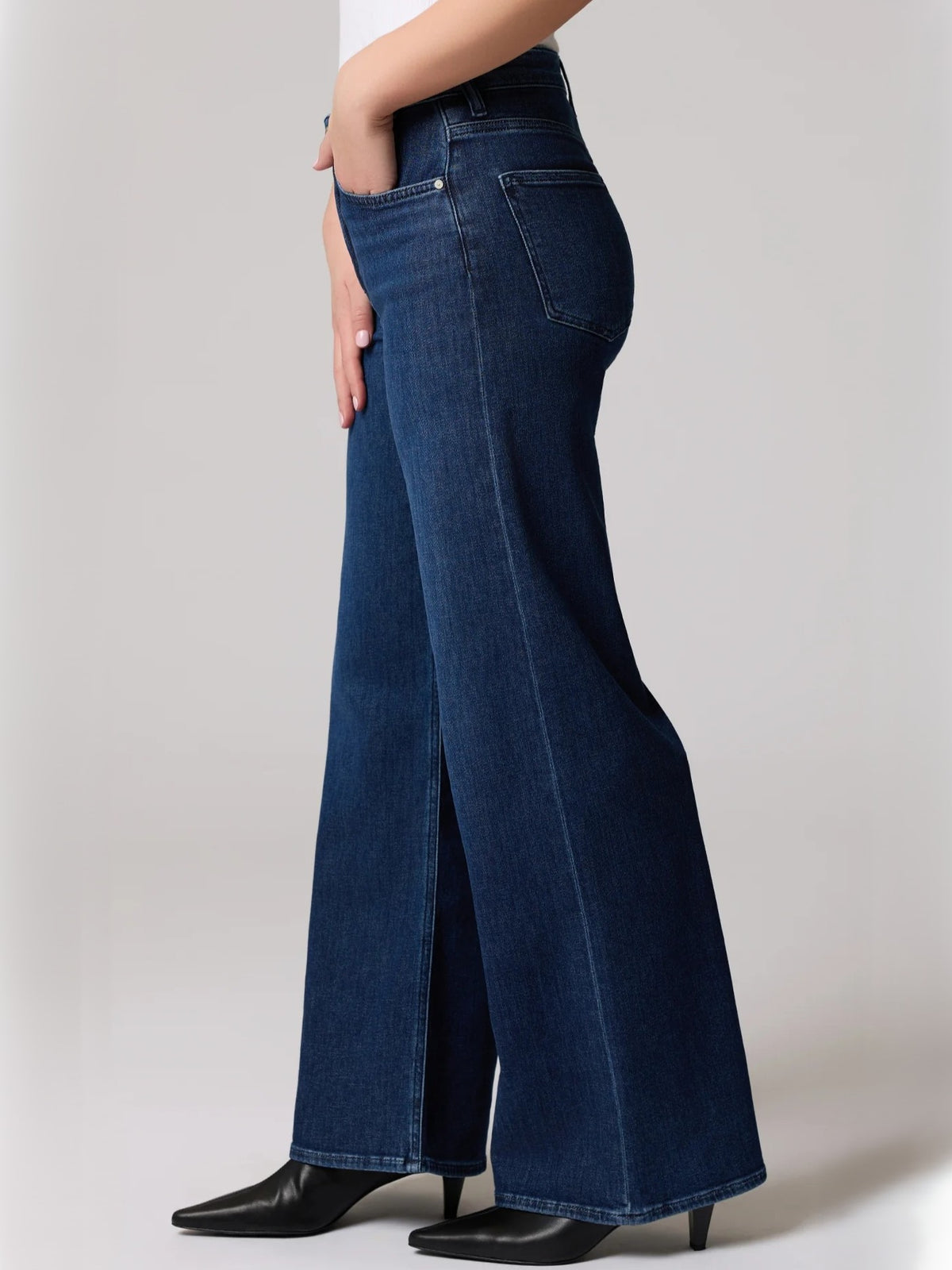 Side view of dark blue wide leg denim jeans styled with black heeled boots