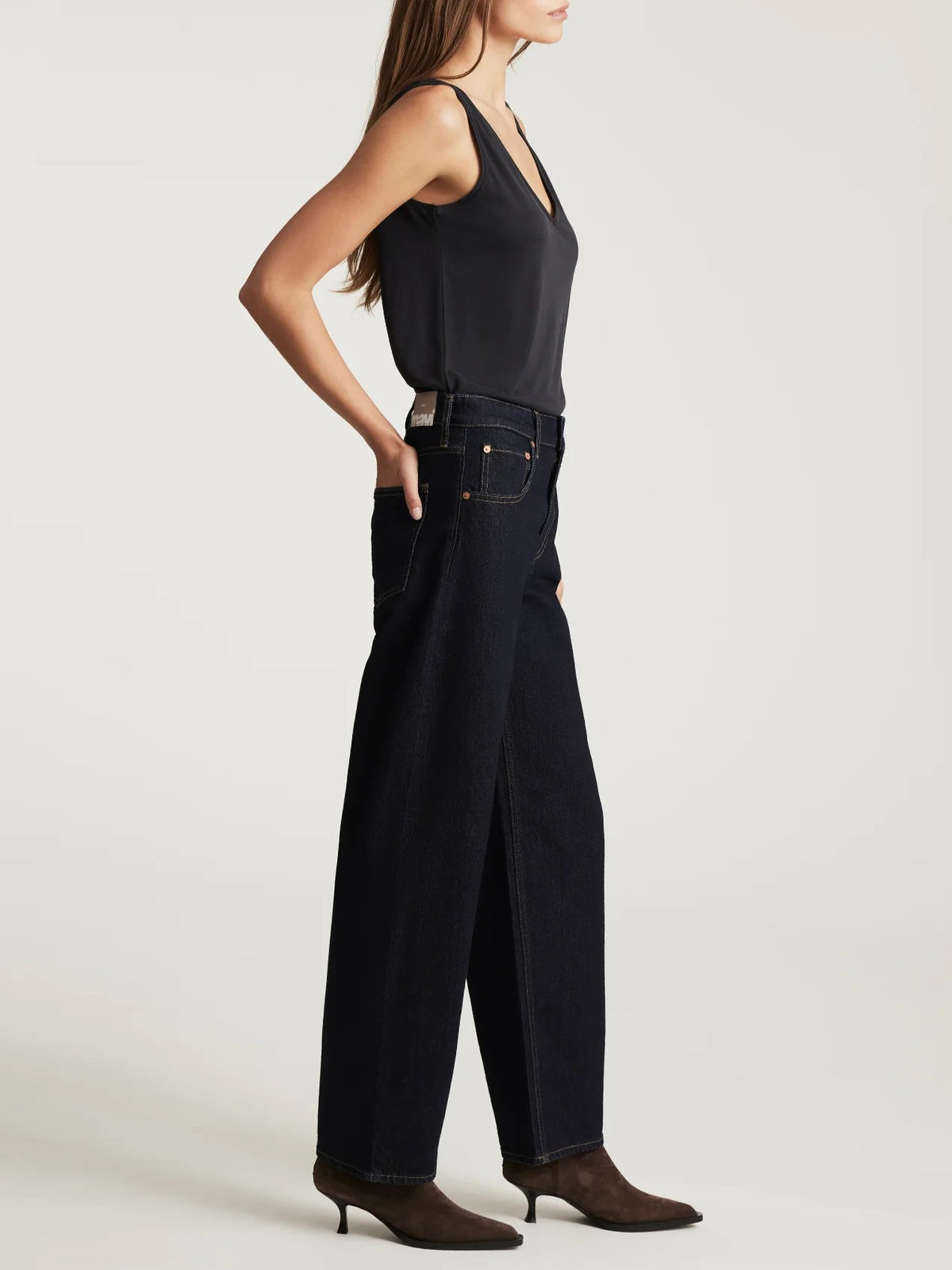 Side view of a sleeveless black top paired with high-waisted wide-leg dark denim jeans and brown heeled shoes.