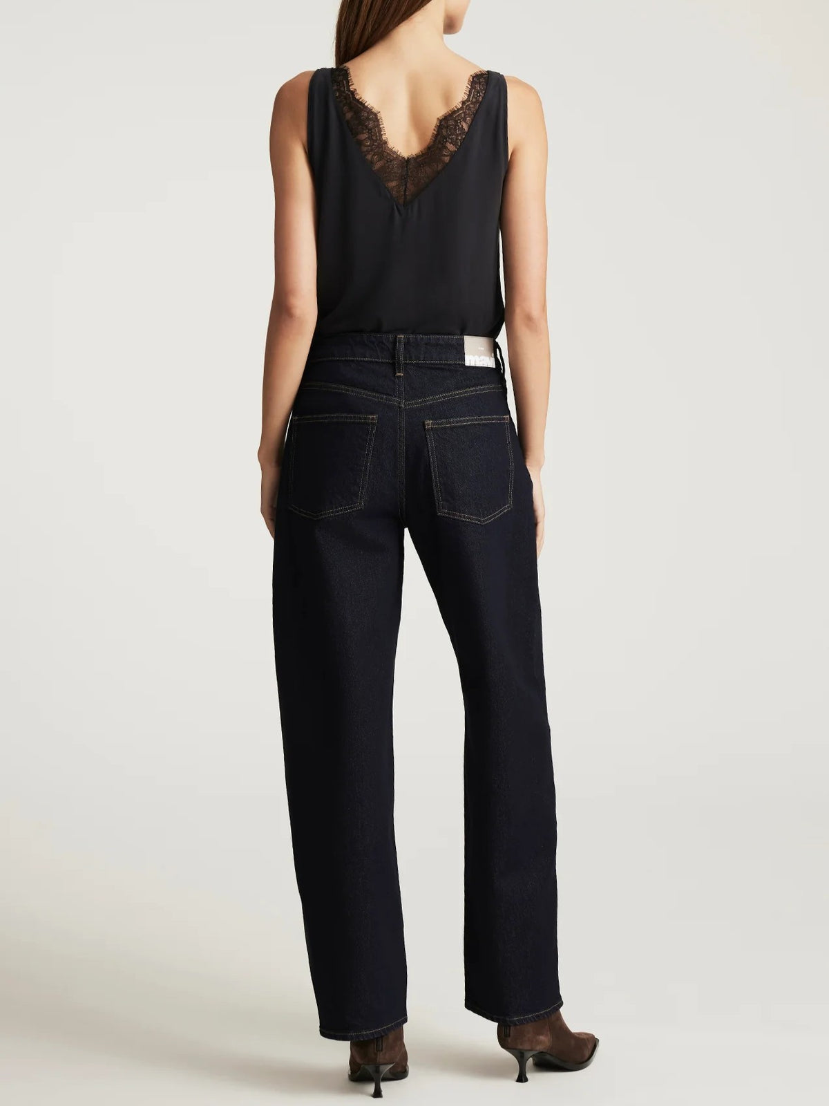 Back view of dark denim jeans paired with a black sleeveless top featuring lace detail on the upper back.