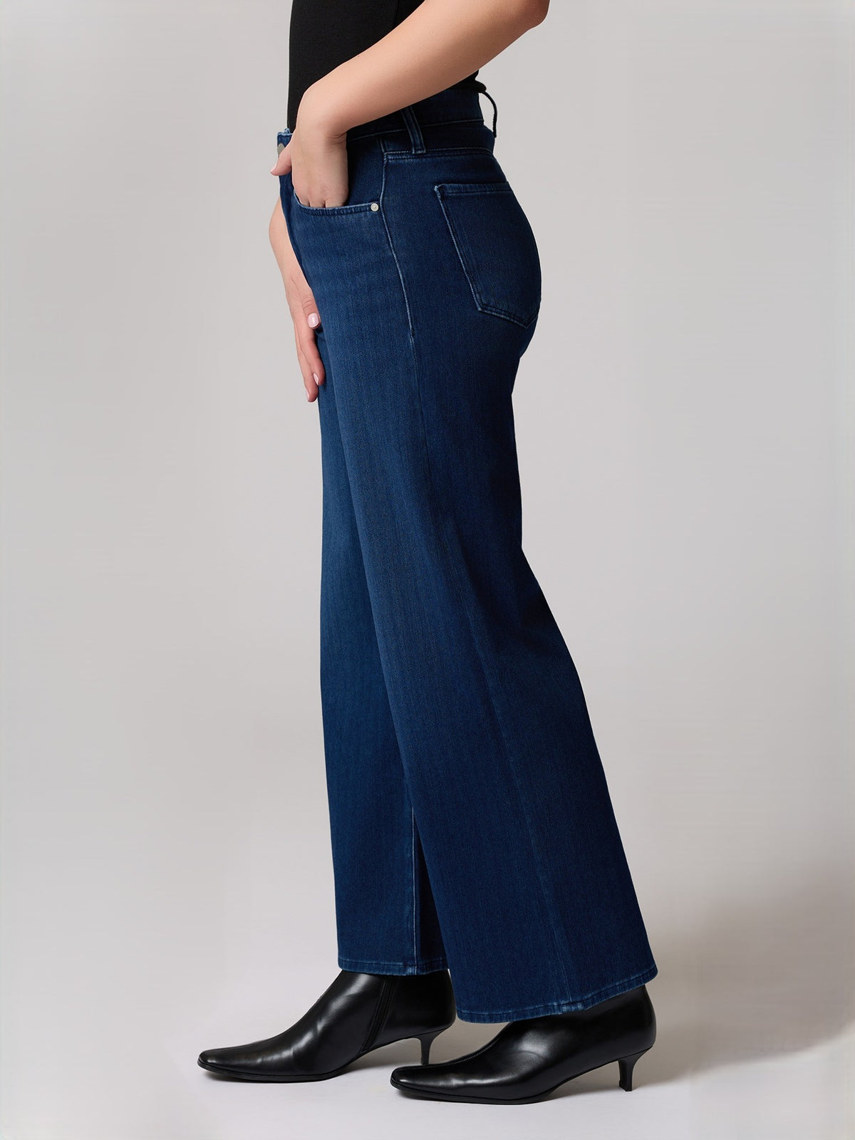 Side view of dark blue wide-leg denim jeans with back pockets and black heeled ankle boots