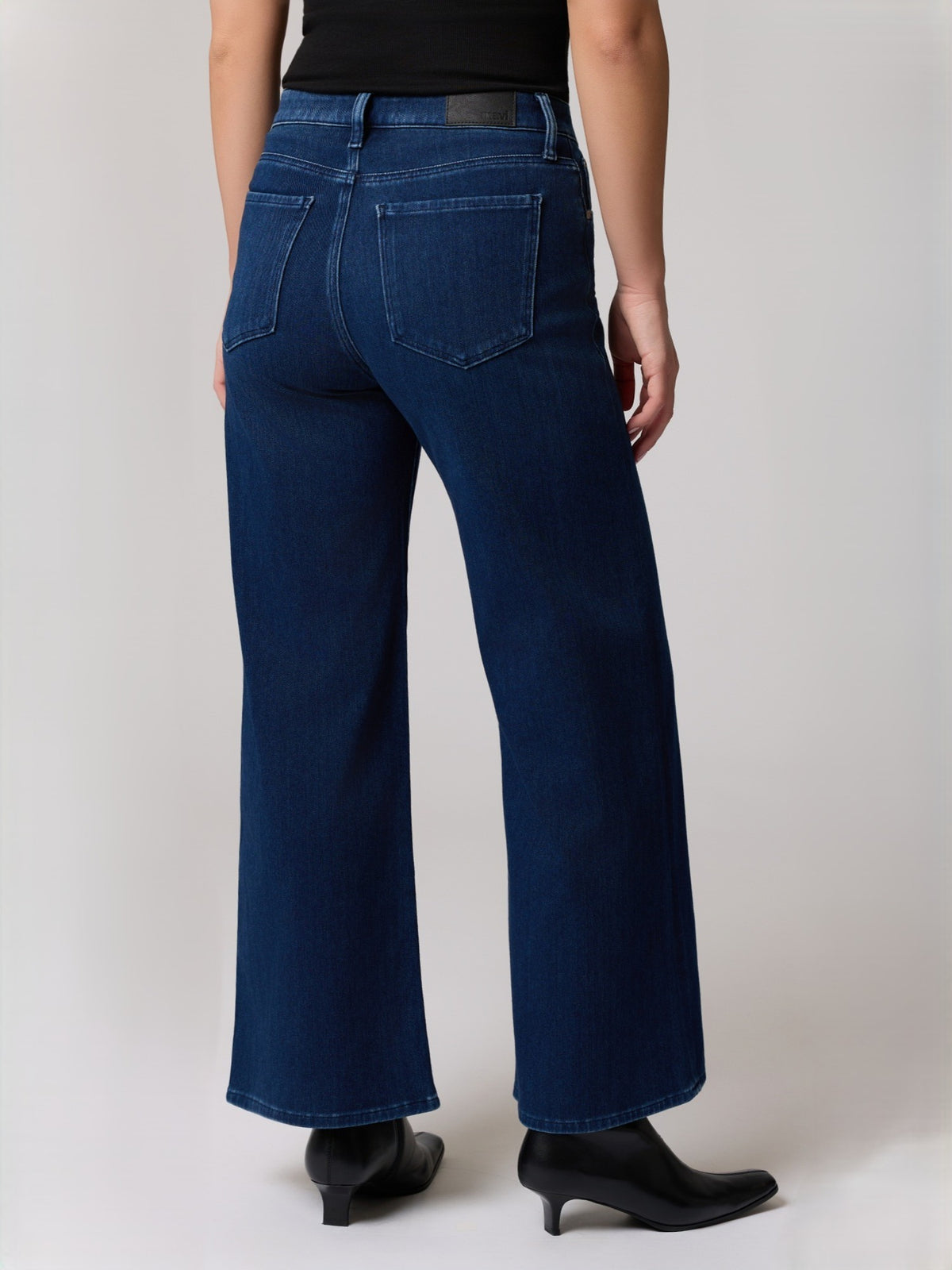 Back view of dark blue wide-leg denim jeans with back pockets and black ankle boots