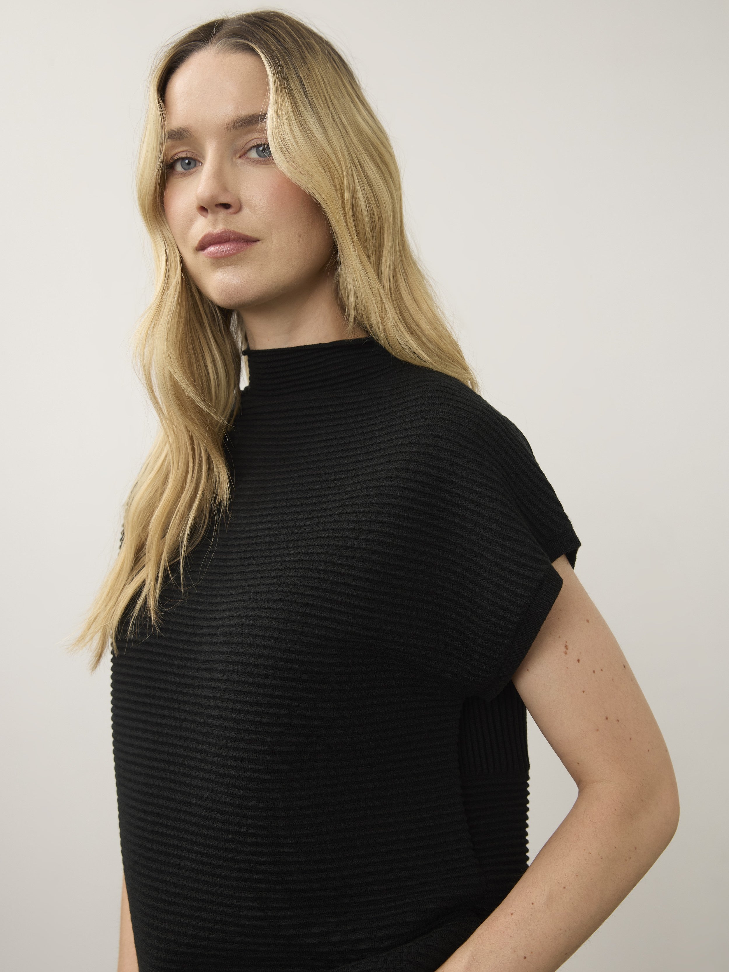 Close-up of a ribbed black sleeveless top with a high neckline on a light background