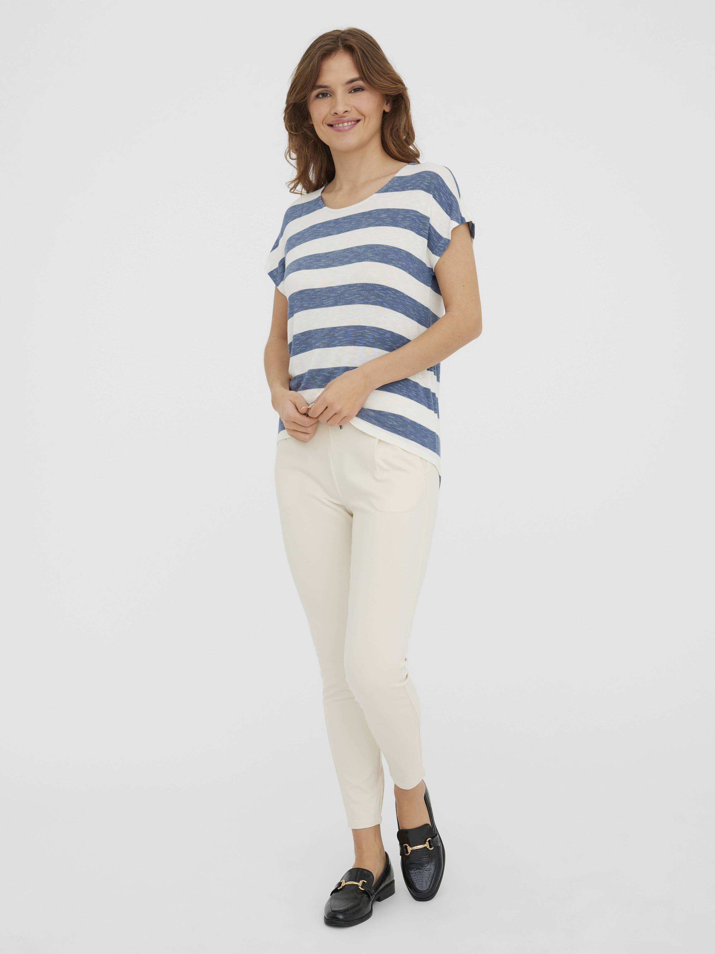 Person wearing a short sleeve blue and white striped top with cream slim pants and black loafers on a plain background