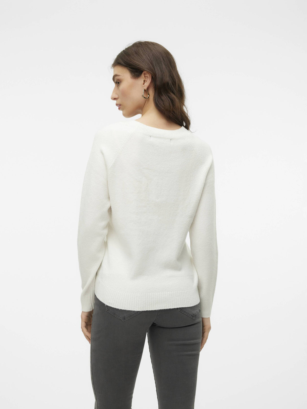 Person shown from behind wearing a white sweater and dark gray fitted jeans against a plain background