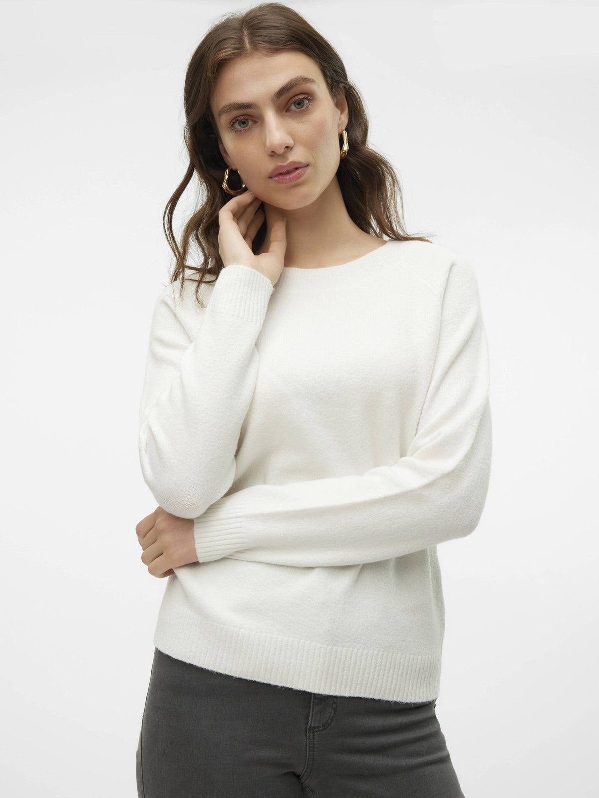 Person in a white long-sleeve sweater and dark pants standing against a plain light background.