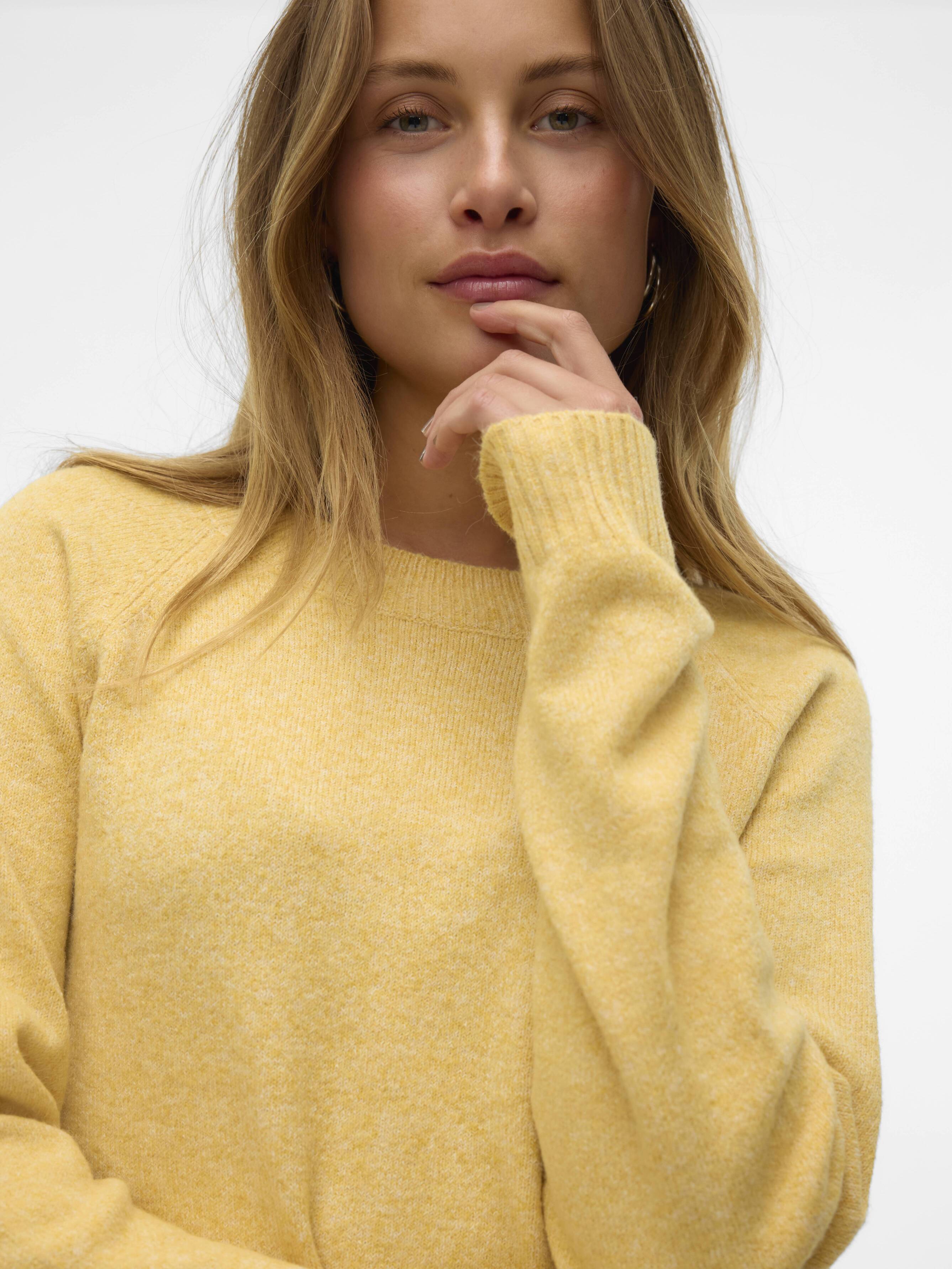 Close-up of a person wearing a soft yellow sweater with a relaxed fit and long sleeves against a plain background.