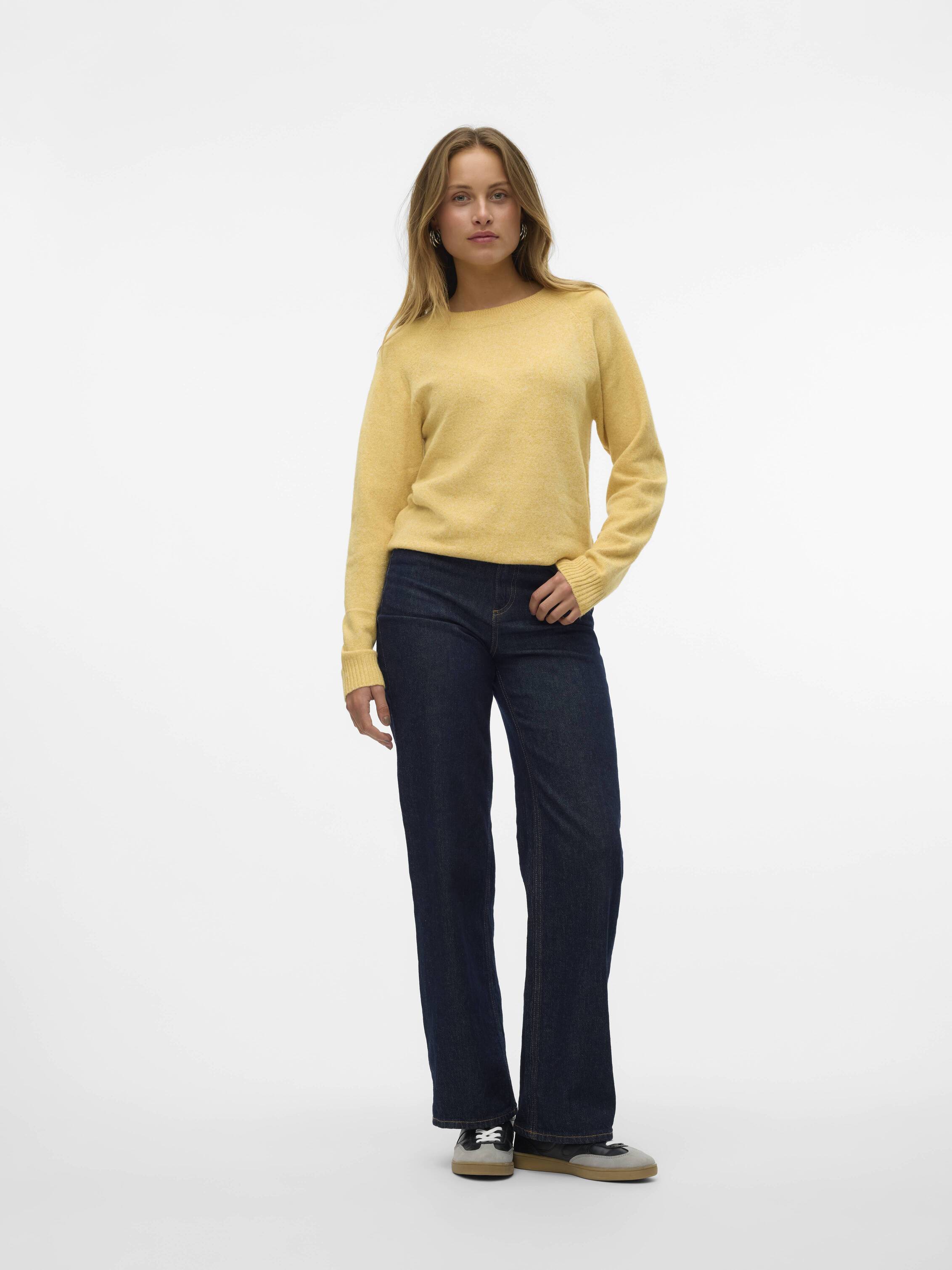 Individual wearing a yellow sweater and dark blue jeans standing against a plain white background