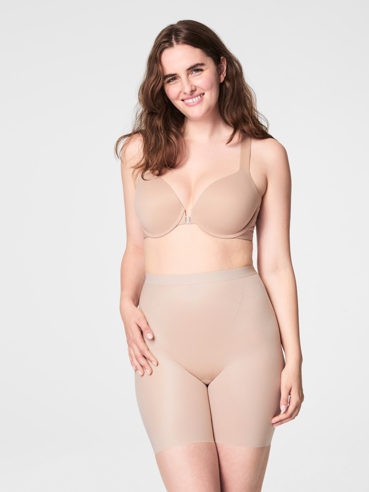 Spanx model wearing beige SPANX Thinstincts® 2.0 Mid-Thigh Shaping Shorts with supportive bra top.