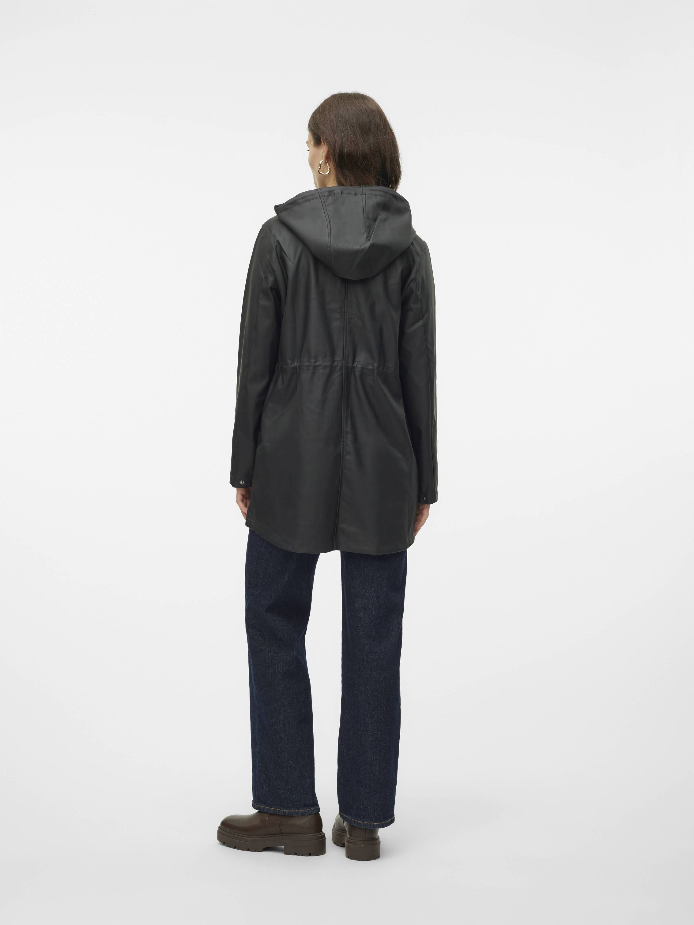 Person wearing a black hooded long jacket paired with dark blue jeans and brown shoes, viewed from the back.