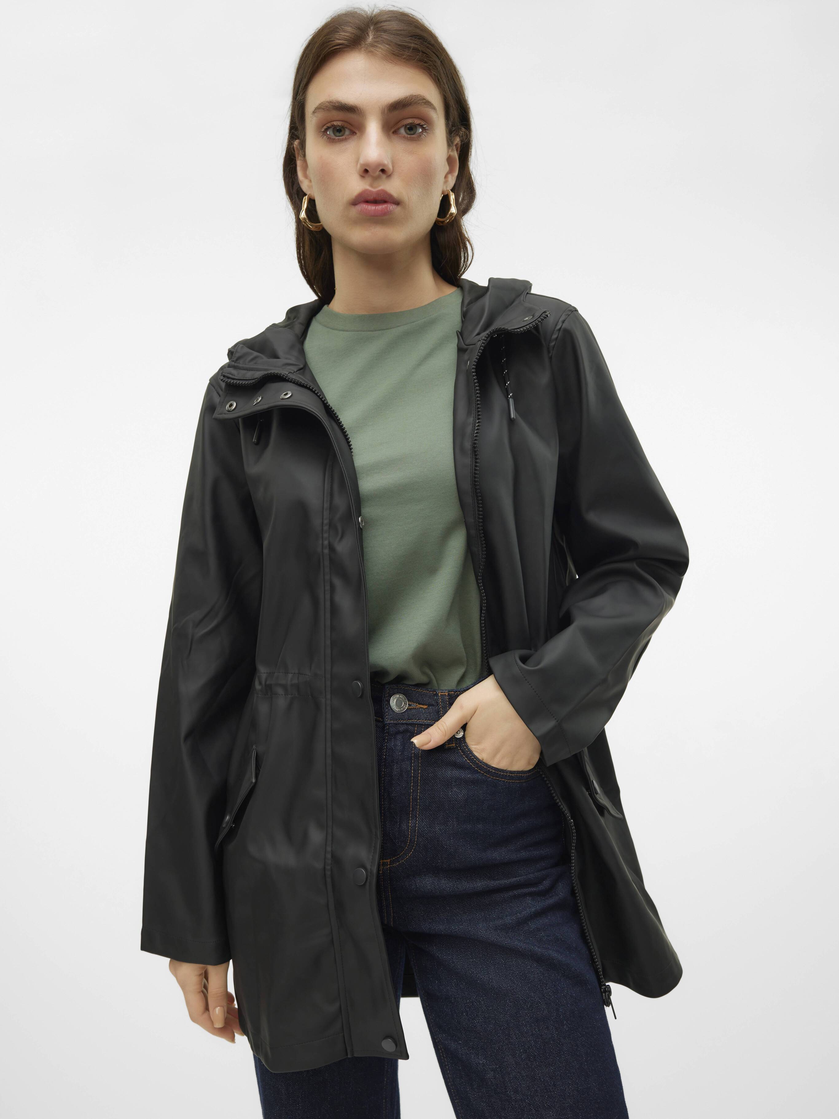 Person wearing a black waterproof jacket over a green top with dark blue denim jeans and gold hoop earrings.