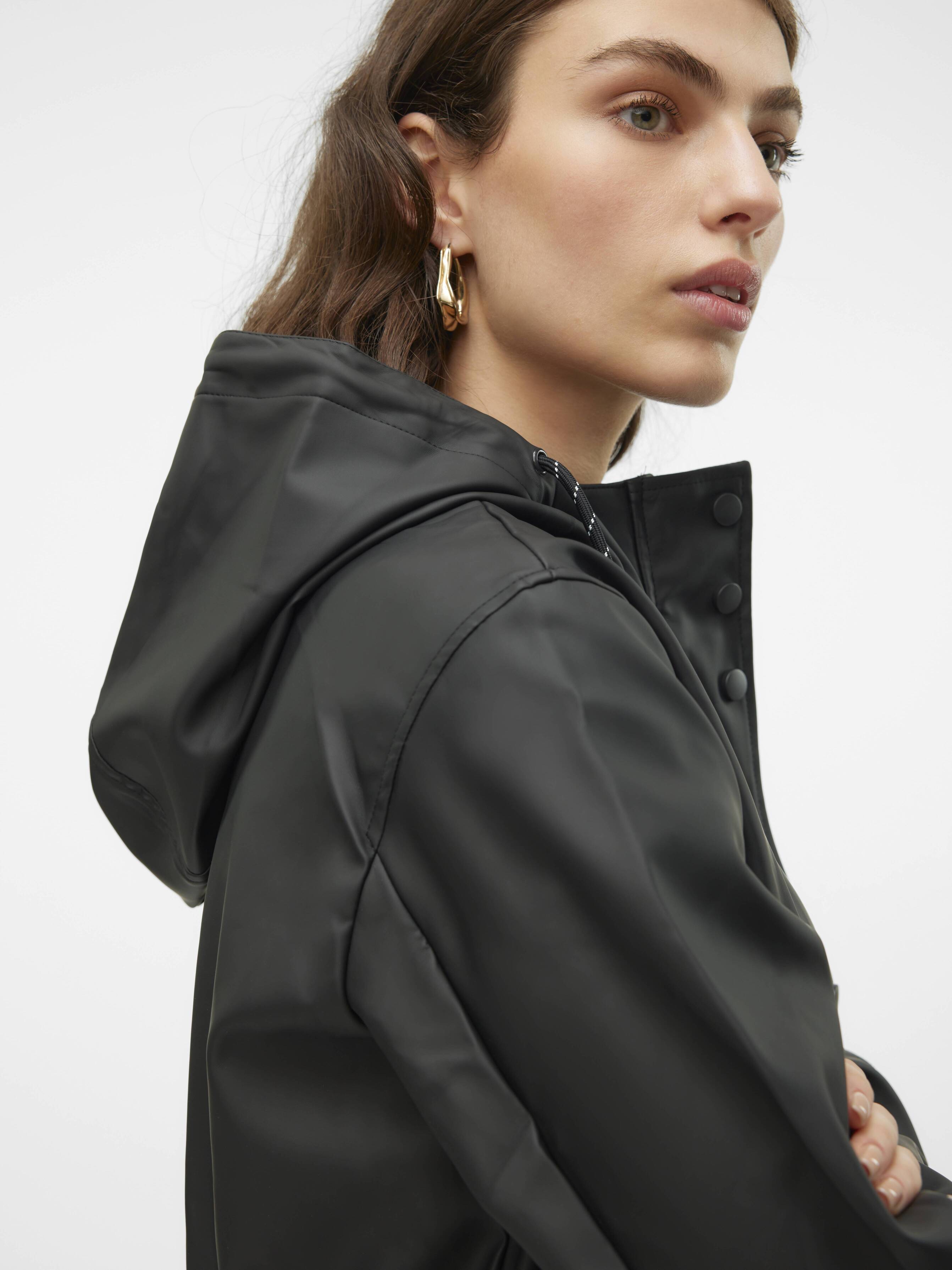 Close-up of a person wearing a black hooded jacket with snap buttons and gold hoop earrings against a white background