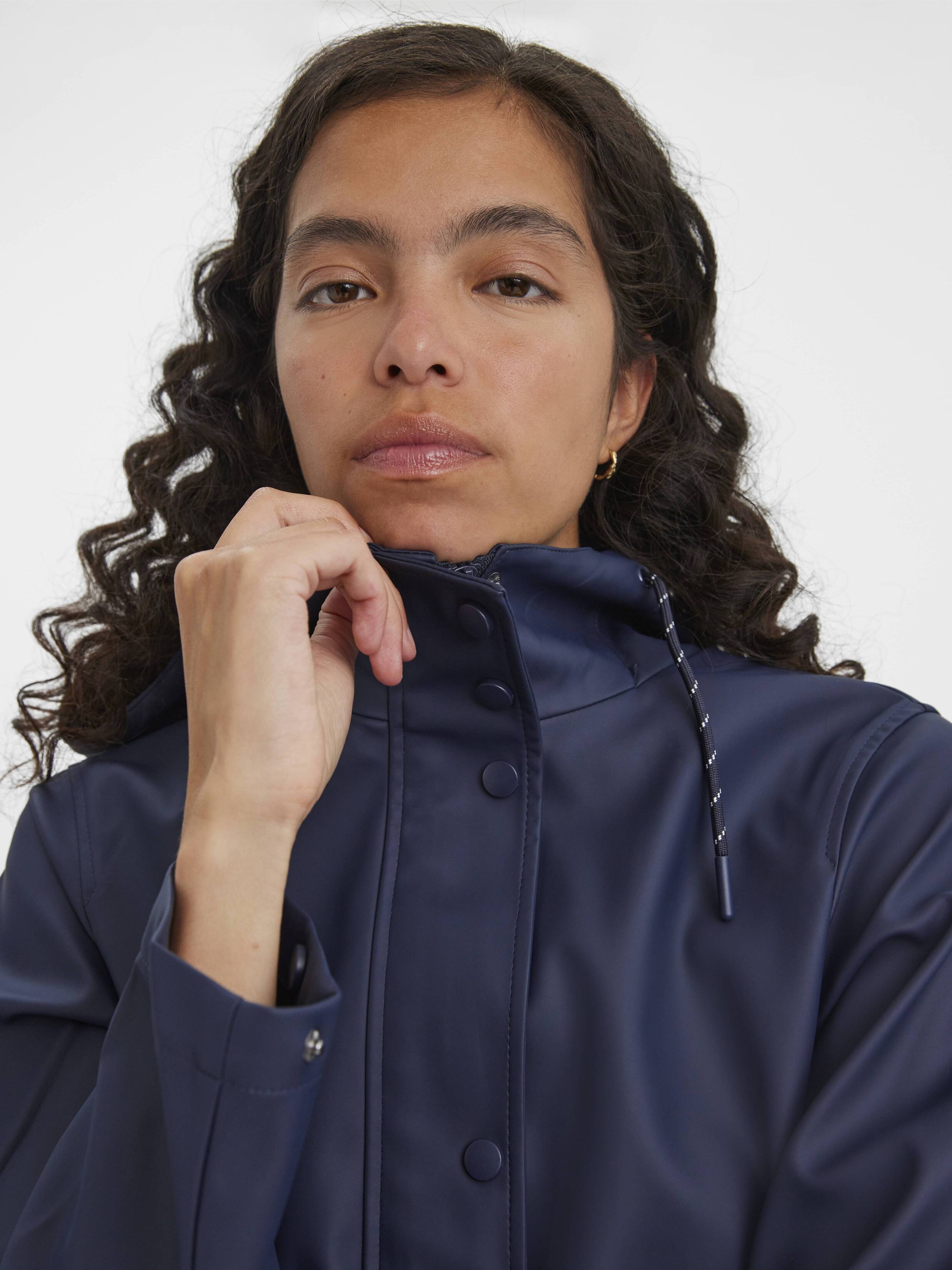 Close-up of a person adjusting the collar of a navy blue waterproof jacket with snap buttons and drawstrings.