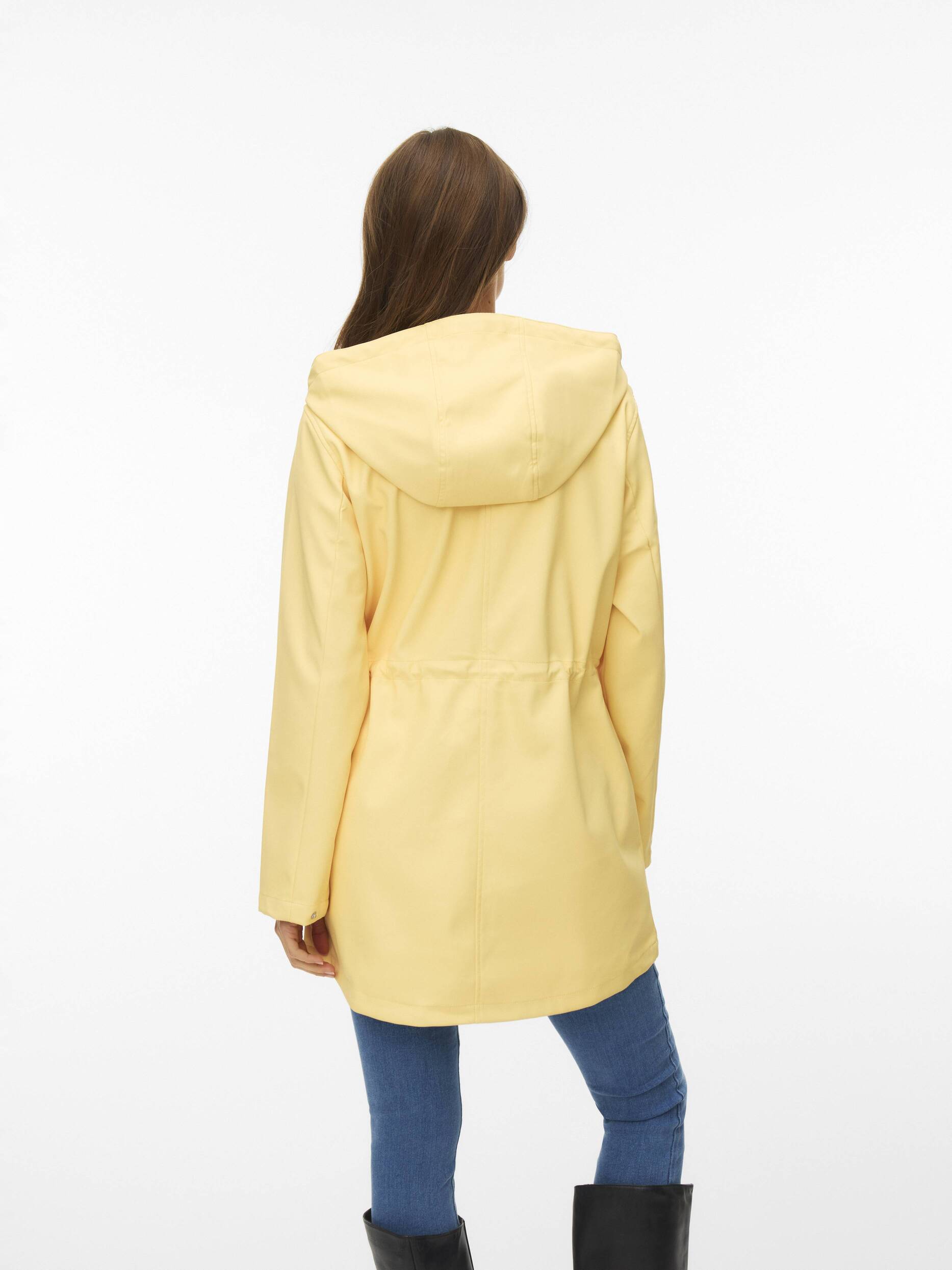 Rear view of a person wearing a light yellow hooded coat with blue jeans and black boots on a white background