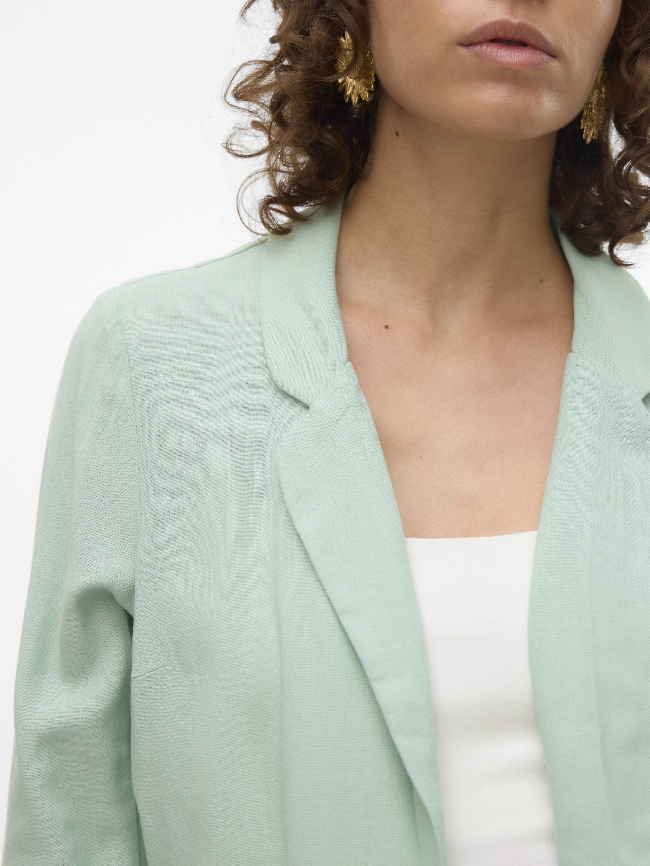 Close-up of a light green Vero Moda Jensen Blazer with notched lapels, worn over a white top and gold earrings.