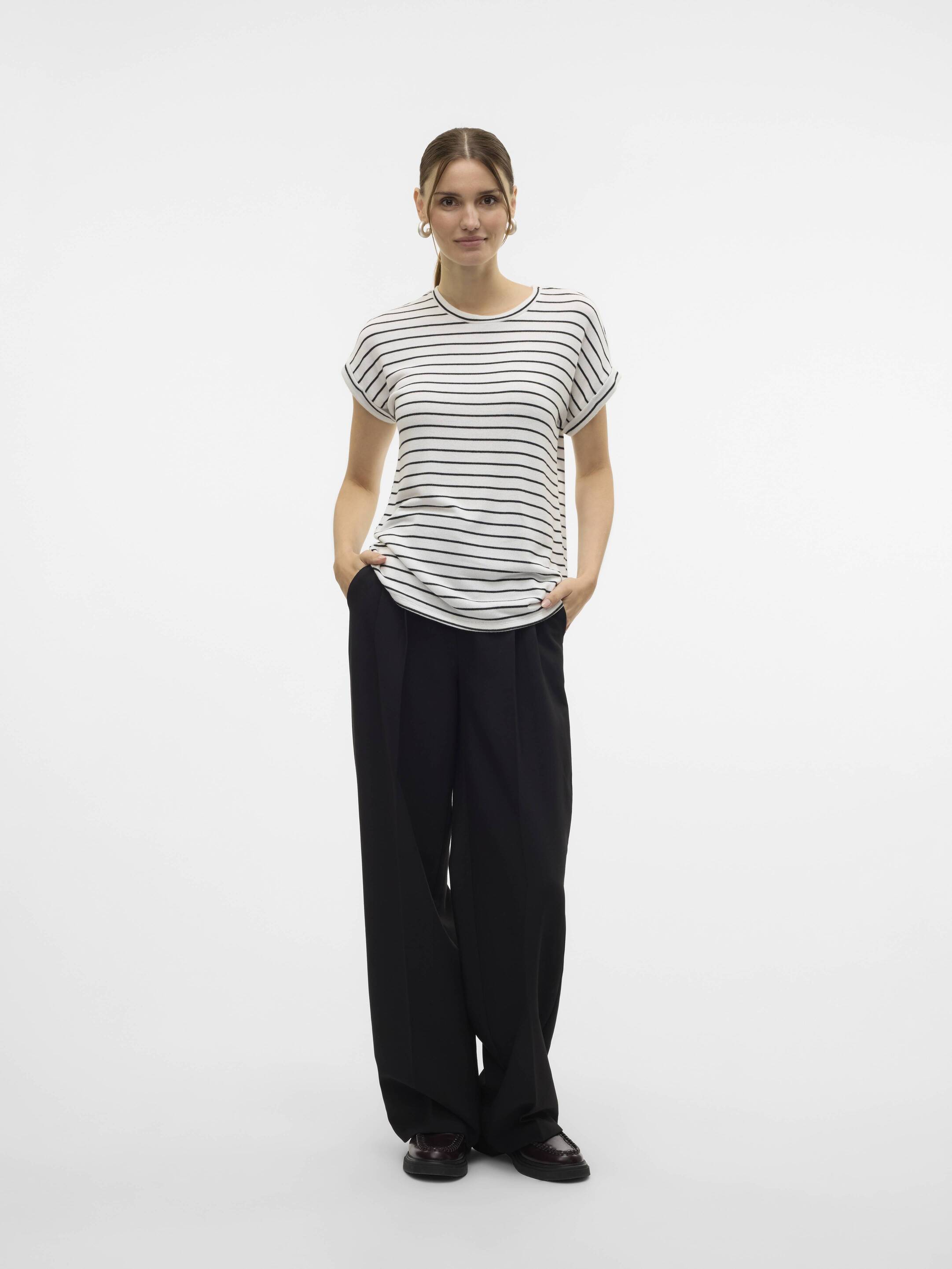 Person in a white and black striped short-sleeve top paired with loose black trousers and dark shoes on a white background