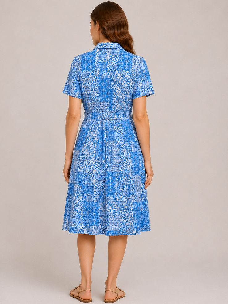 Back view of short-sleeve blue patterned dress with collar and pleated skirt, paired with flat sandals.