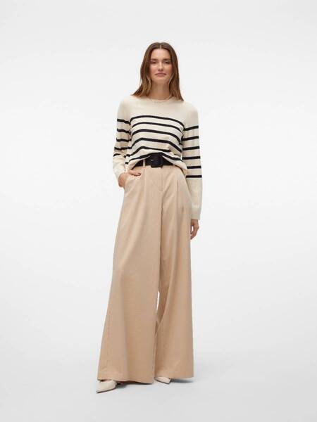 Person wearing a cream and black striped sweater paired with wide-leg beige trousers and white shoes.