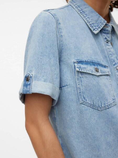 Close-up of a light blue denim short-sleeve shirt with a buttoned chest pocket and rolled sleeve detail.