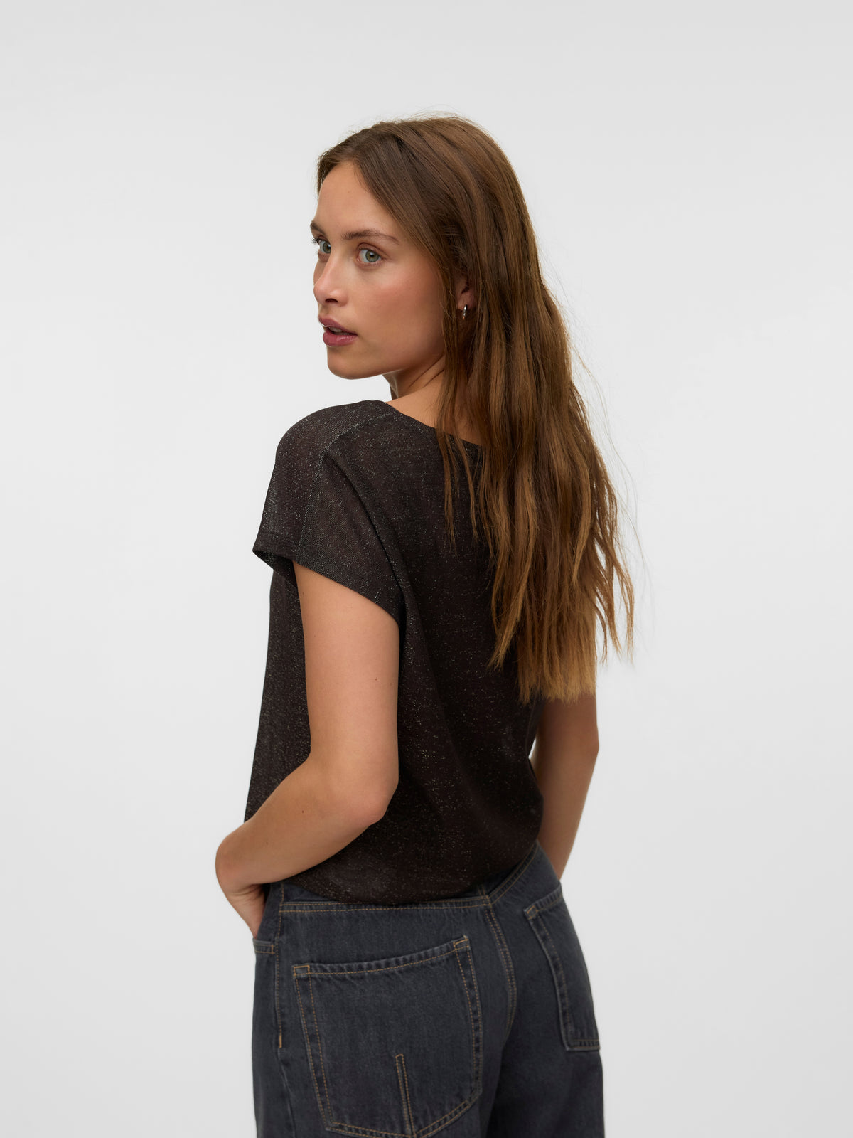 Side view of a woman in a dark brown top and dark denim jeans against a light background