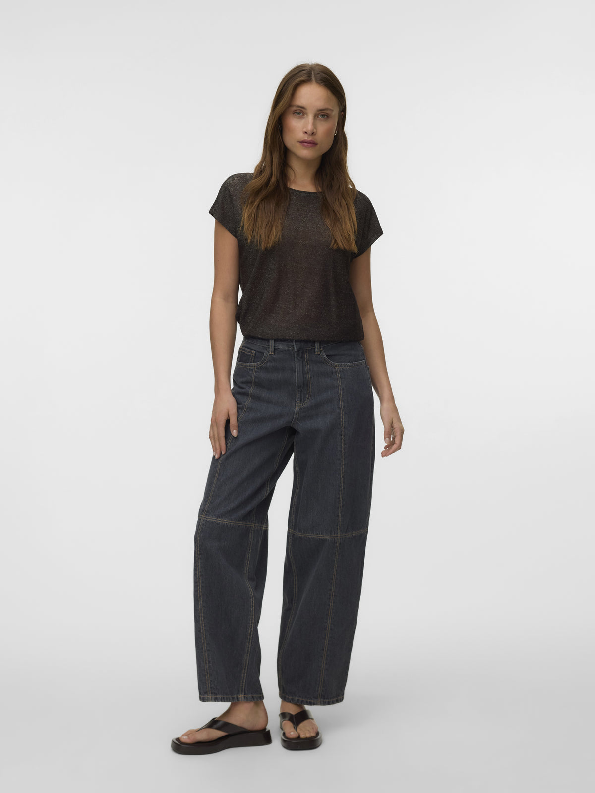 Dark gray T-shirt with wide-leg dark denim jeans and black sandals against a light gray background