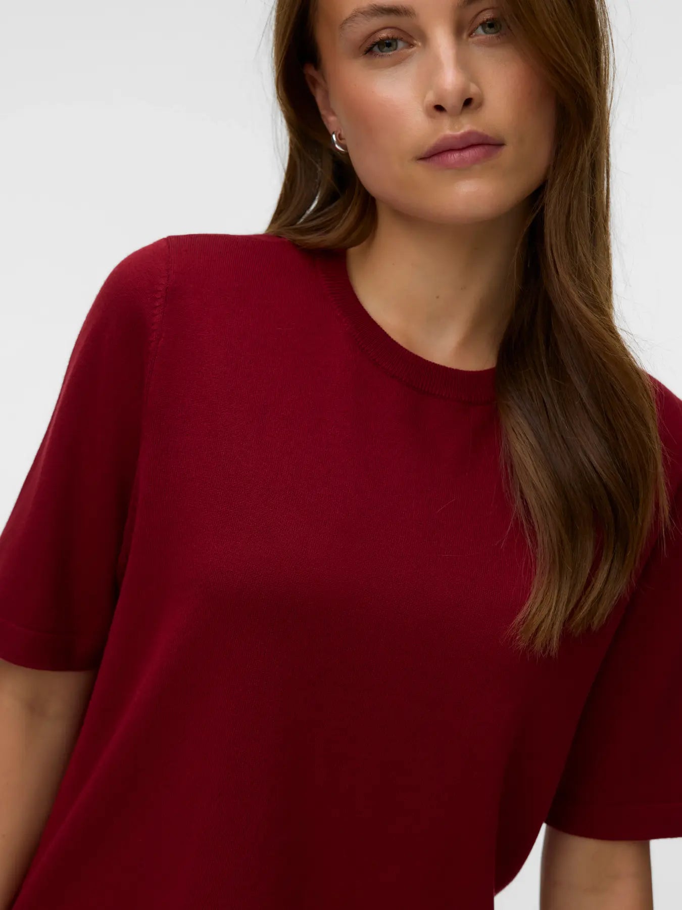 Close-up of a person with long brown hair modeling a plain red short-sleeve knit top against a white background.
