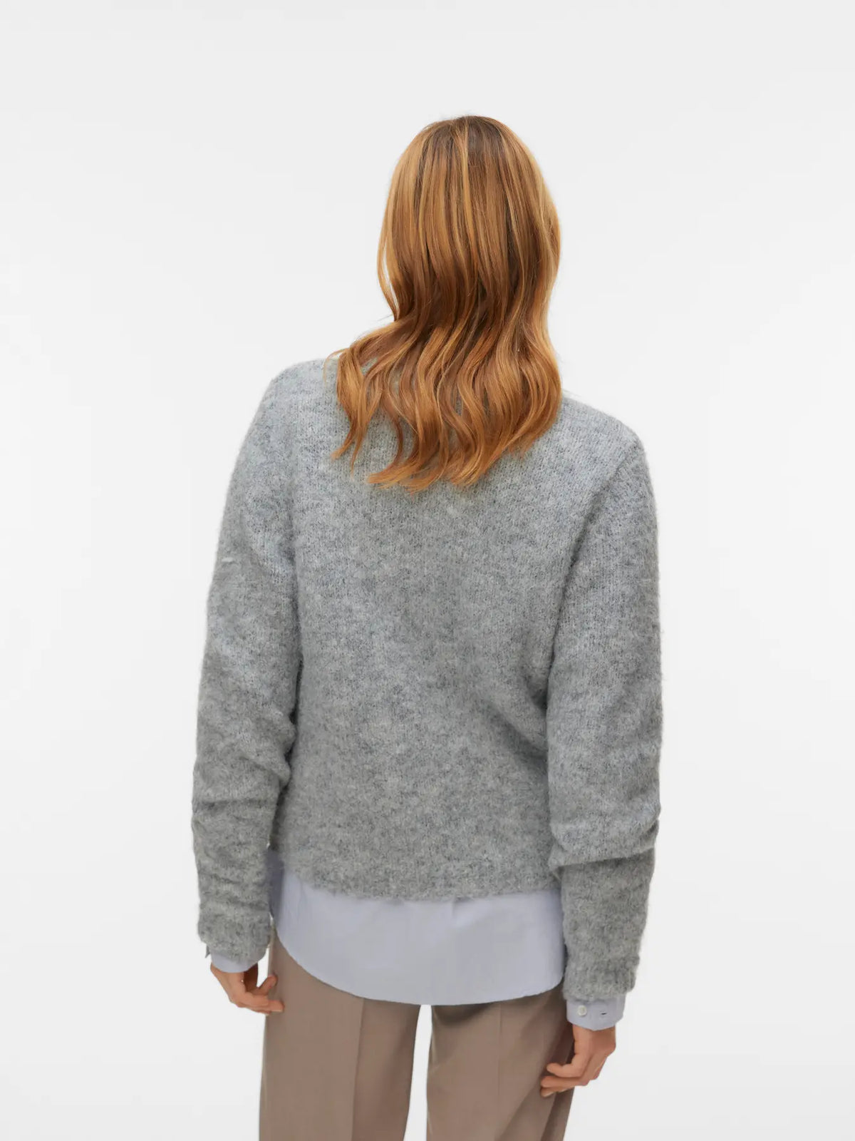 Back view of a person wearing a grey fuzzy sweater layered over a light shirt and beige trousers.