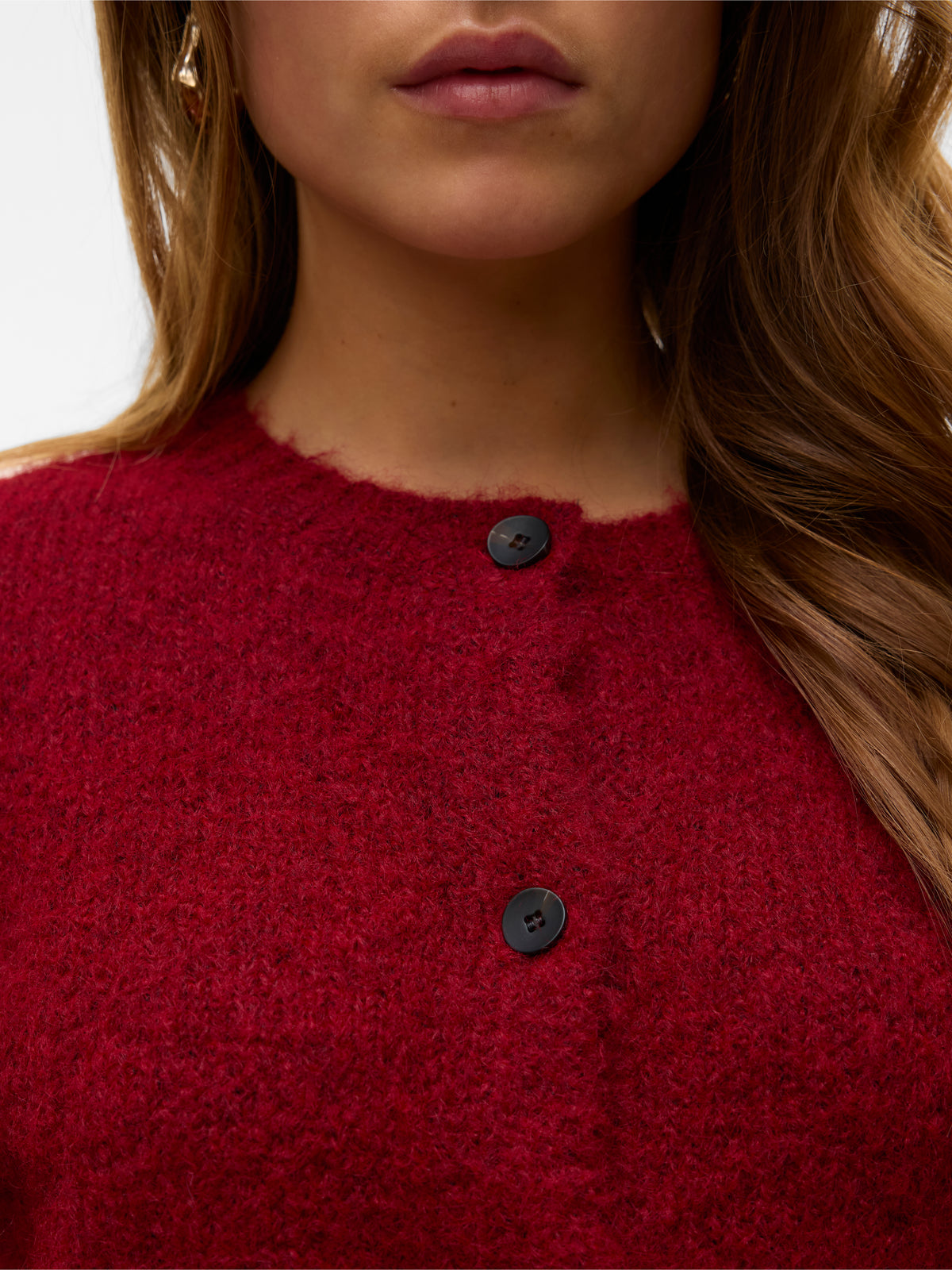 Close-up of a red textured sweater with black buttons and long brown hair partially visible on one side.