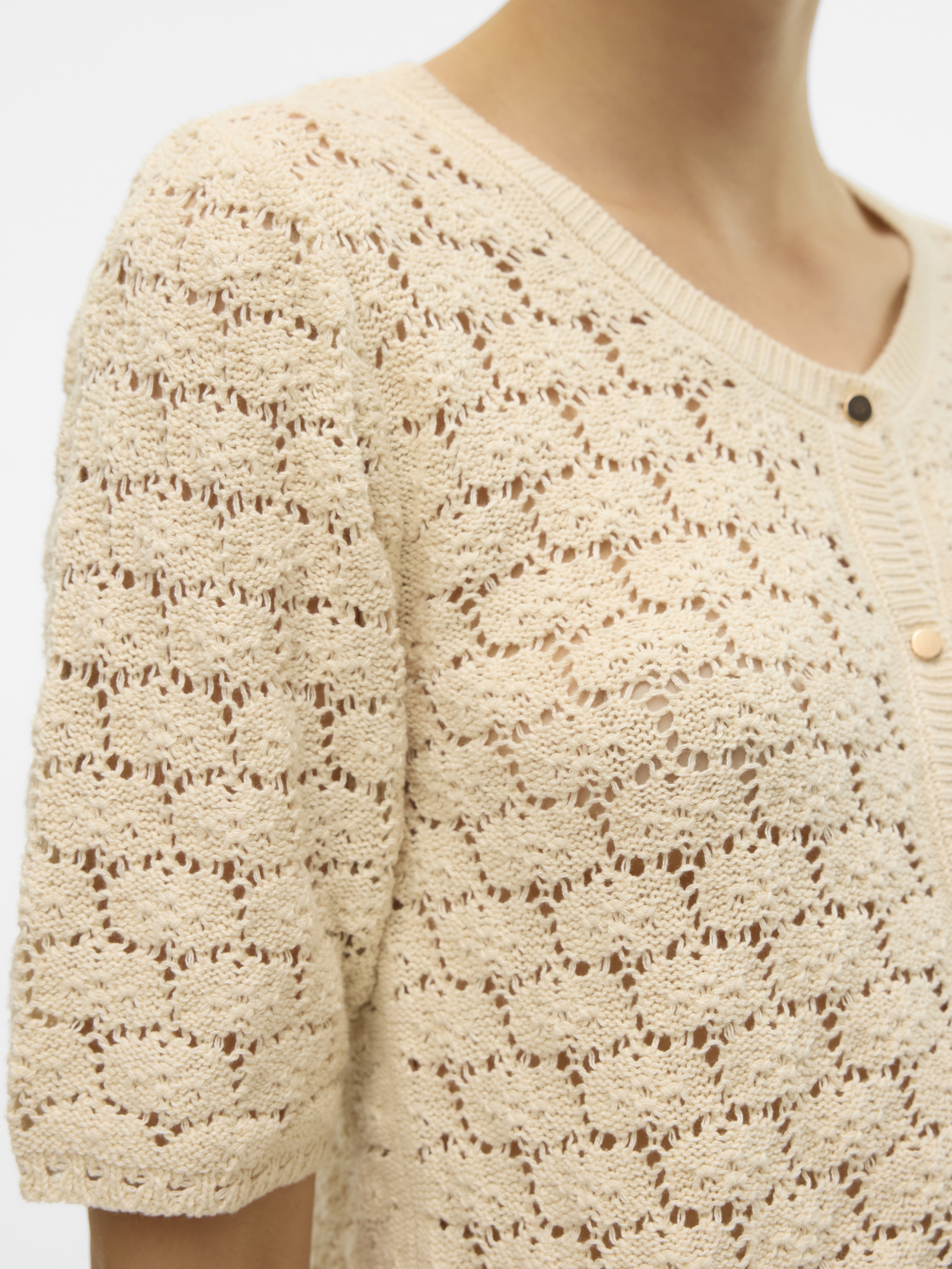 Close-up of an off-white crochet knit top with short sleeves and a round neckline featuring small buttons.