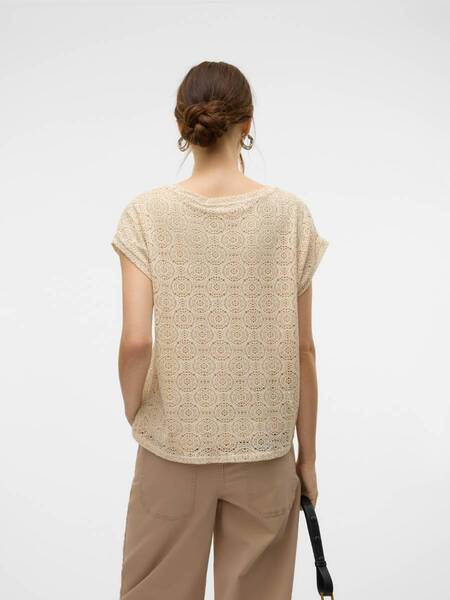 Beige crochet short-sleeve top with circular patterns paired with light brown loose trousers and a black handbag strap.