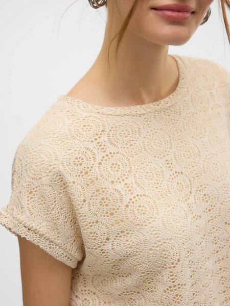 Close-up of a beige crochet knit top with circular patterns and short rolled sleeves on a light background