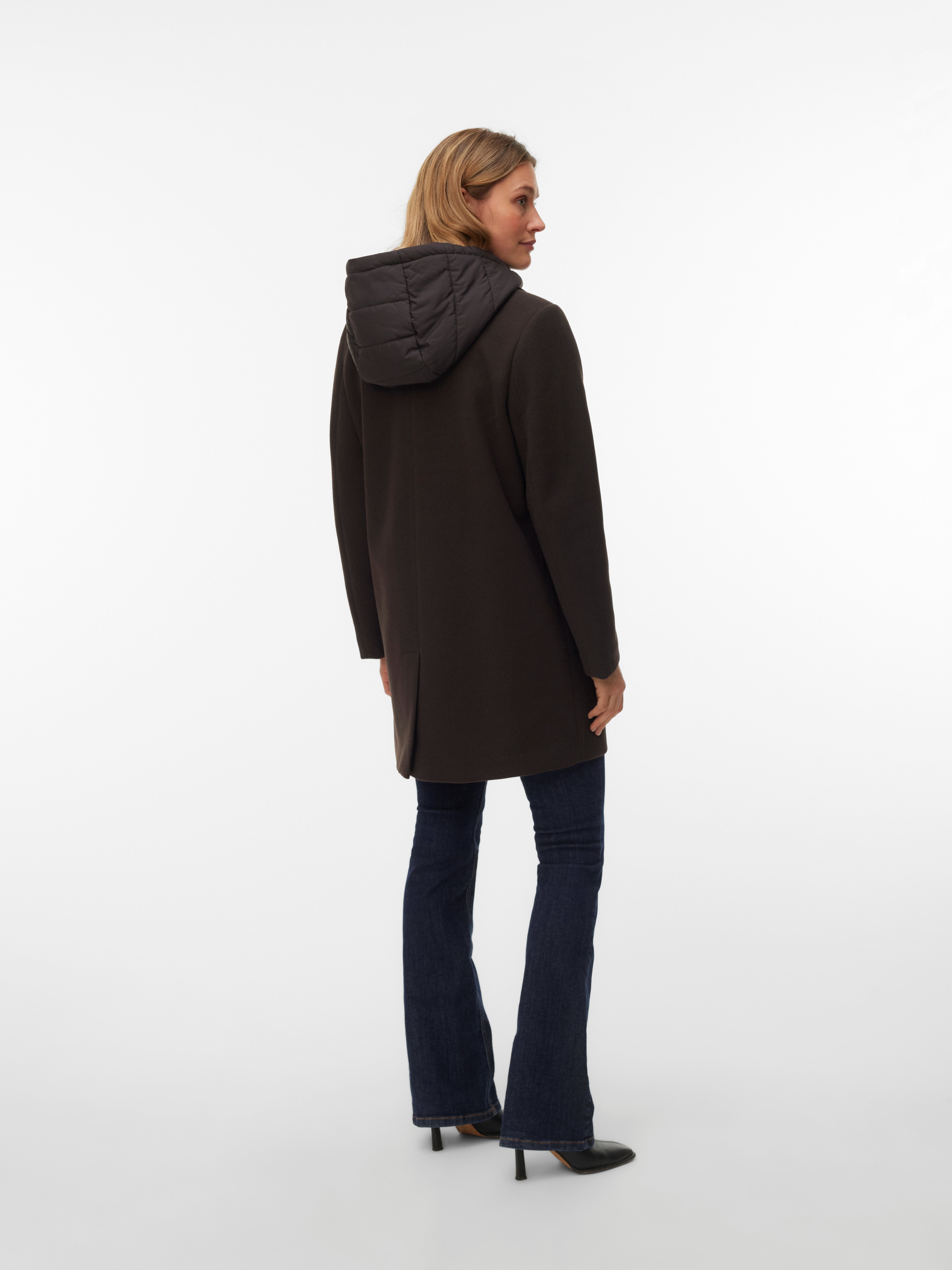 Long dark coat with a quilted hood paired with dark denim jeans and pointed black heels on a white background.