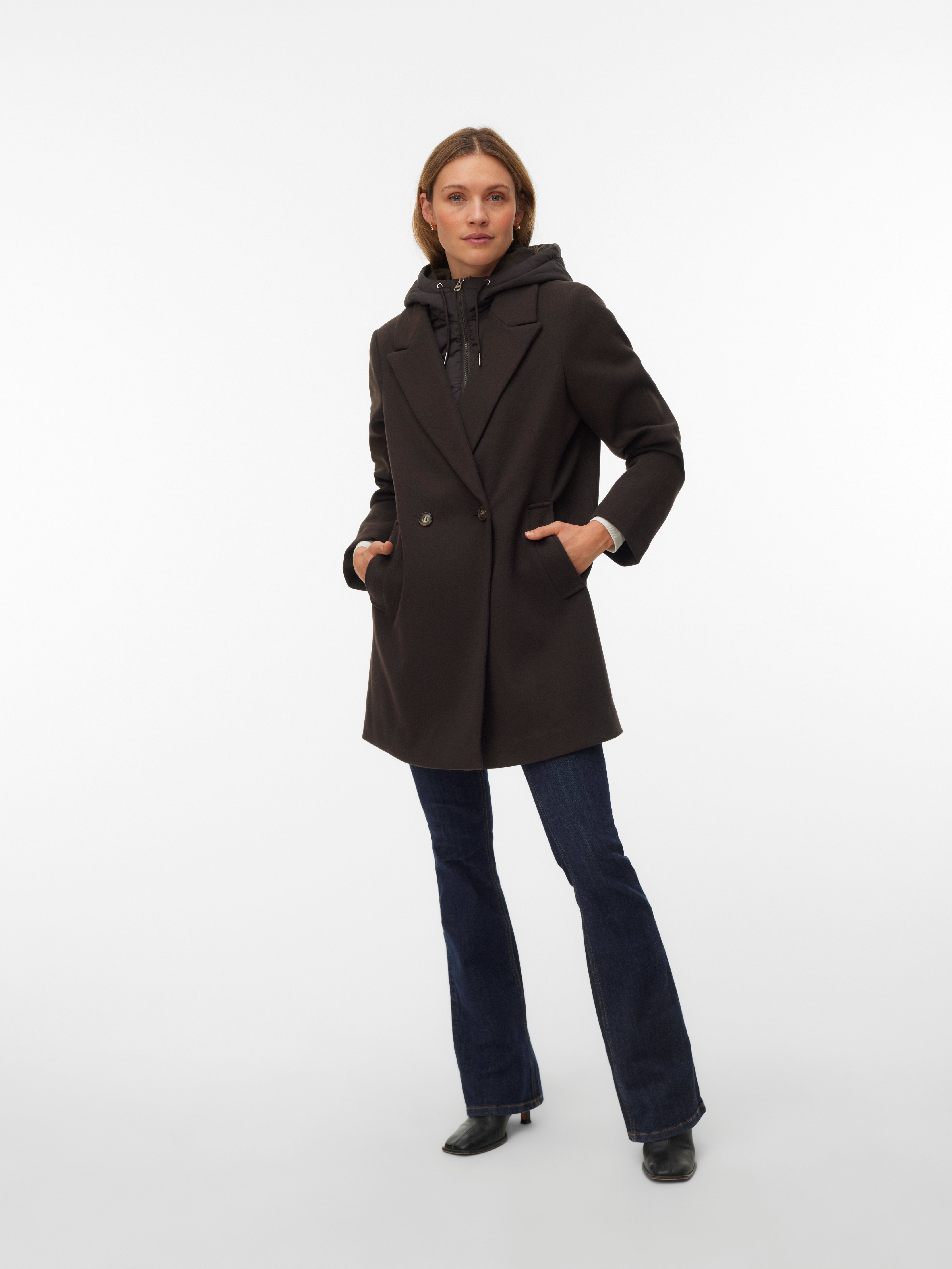 Black double-breasted coat layered over a black hooded jacket paired with dark blue flared jeans and black boots.