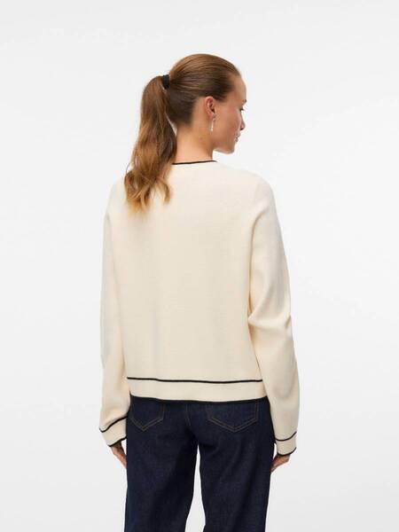 Back view of a person wearing a beige sweater with black trim and dark denim jeans against white background