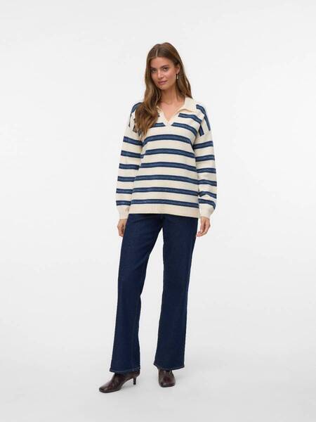 Person standing in a cream and navy striped sweater with dark blue denim pants and brown heeled shoes