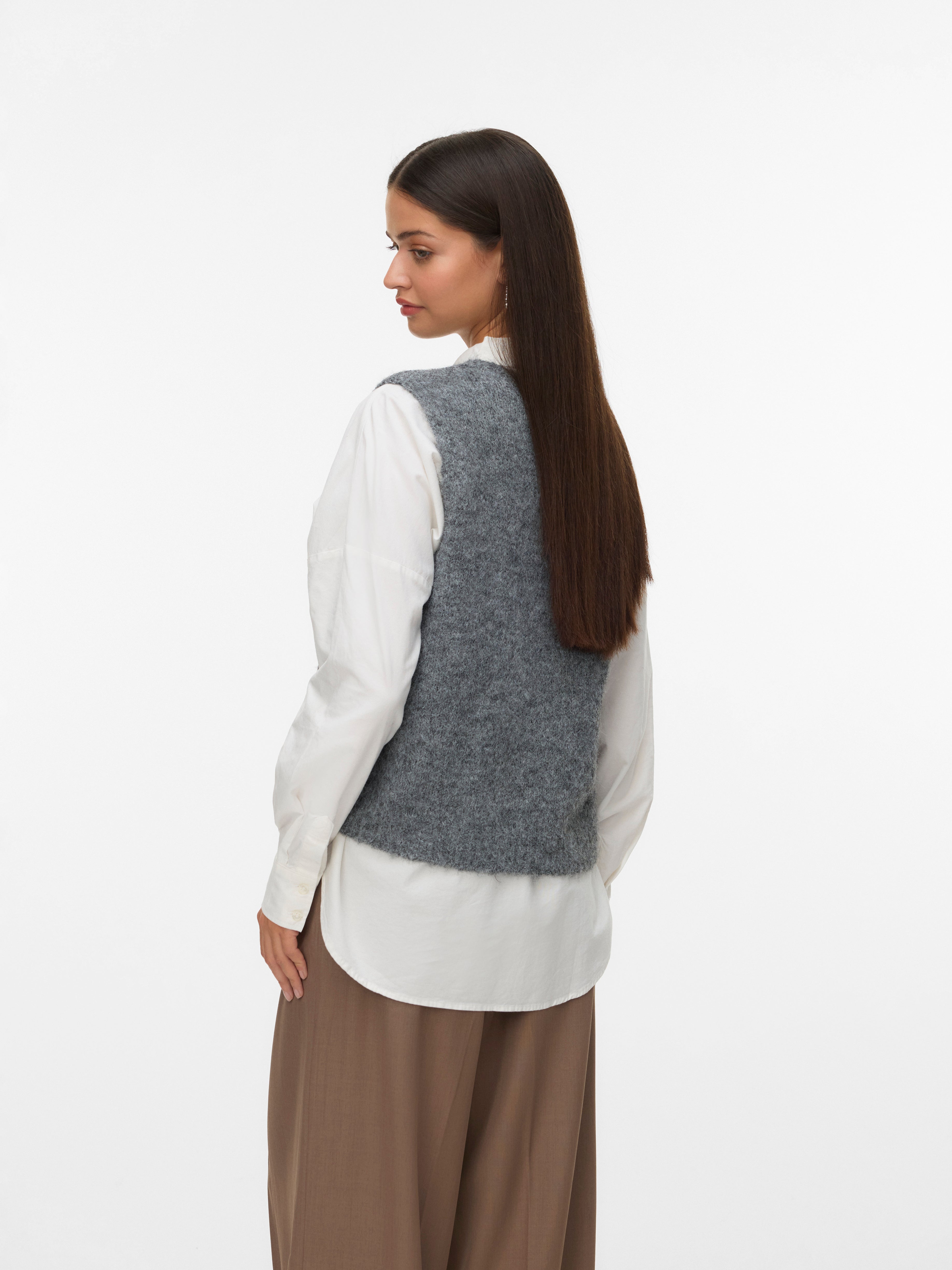 Back view of a gray knitted vest layered over a white long-sleeve shirt and paired with brown wide-leg trousers