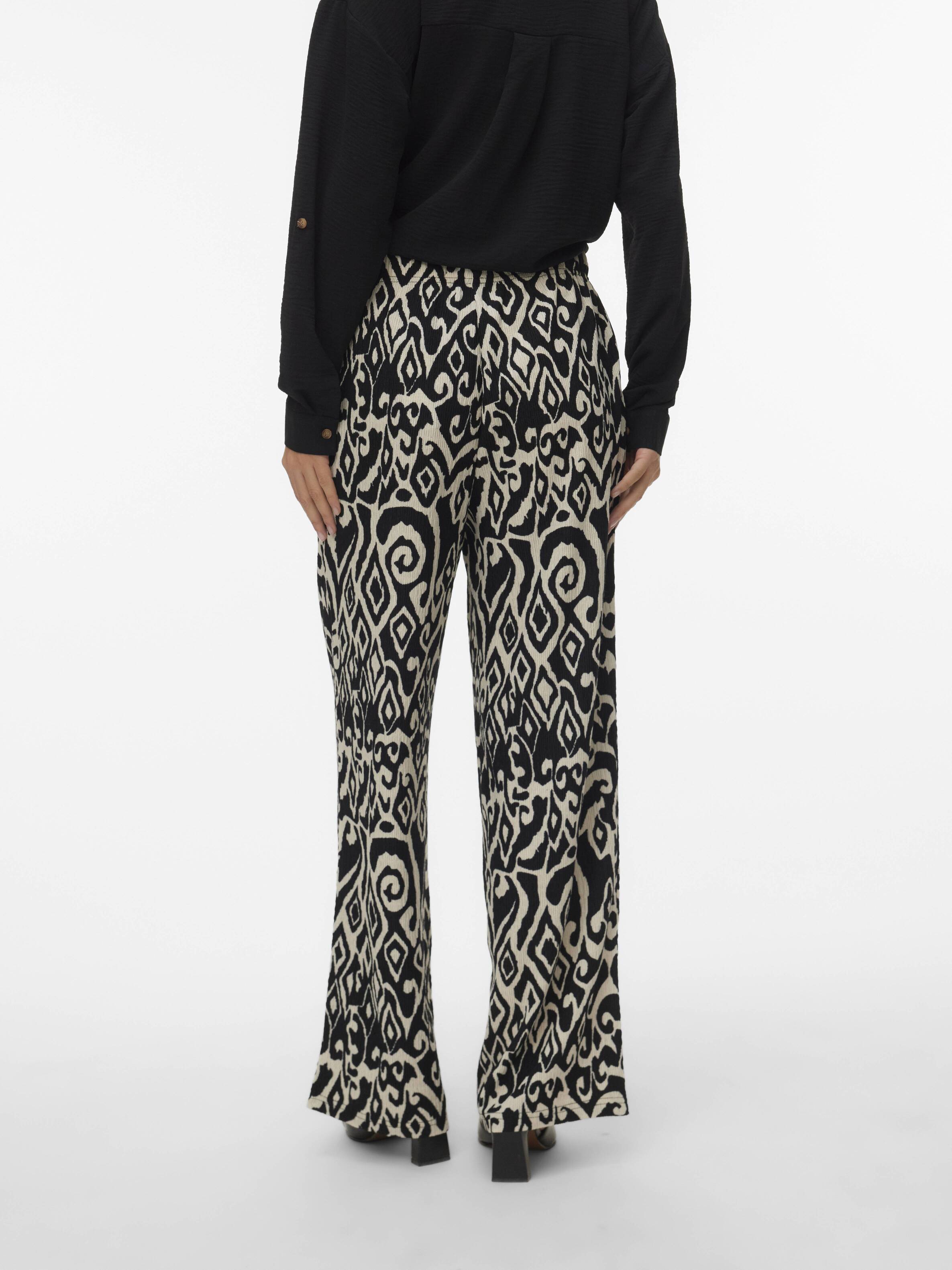 Person standing wearing black and beige patterned wide-leg pants and a black long-sleeve top shown from the back