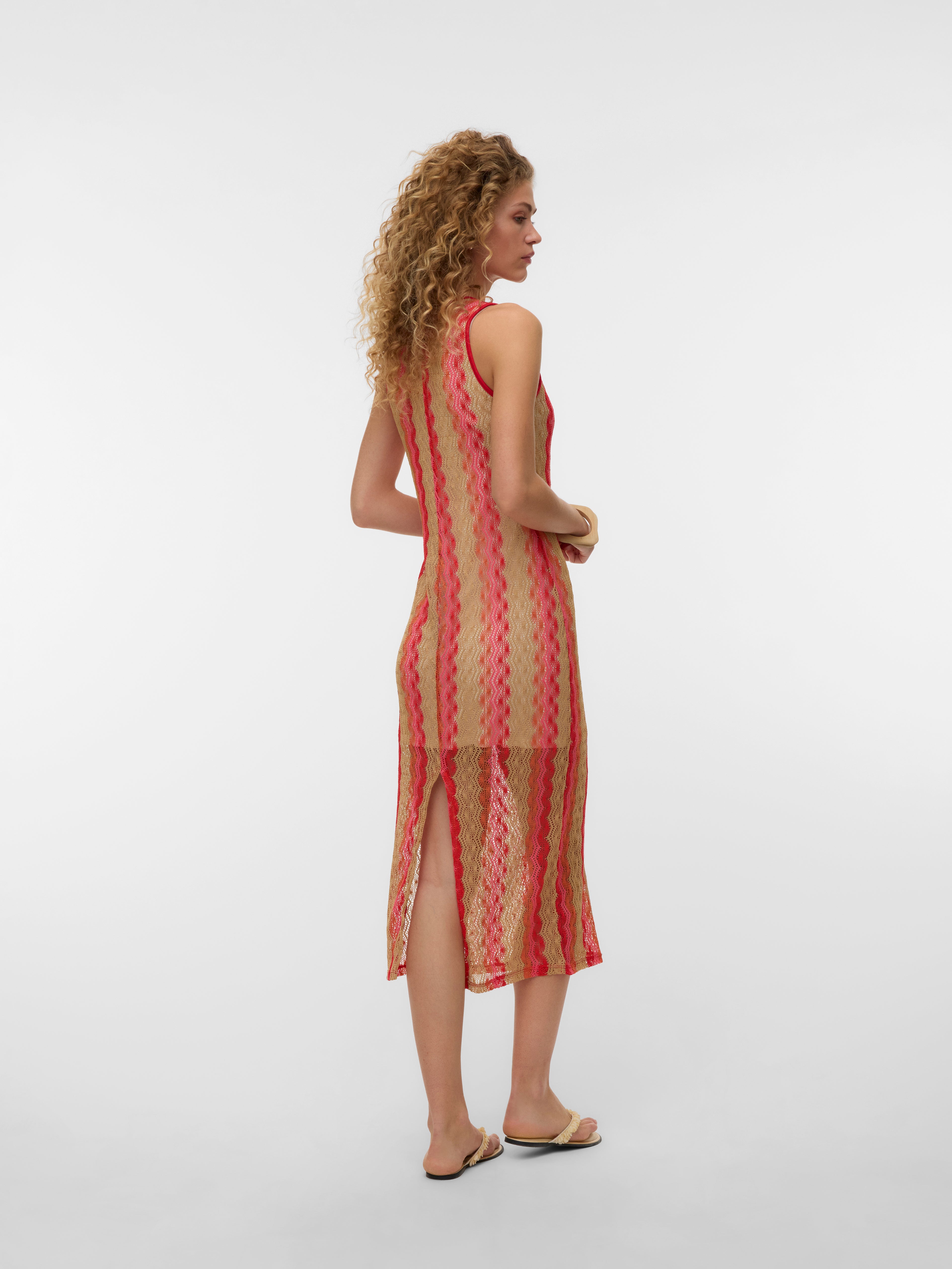 Semi-transparent striped sleeveless dress in beige and red with a back slit, paired with beige flat sandals.