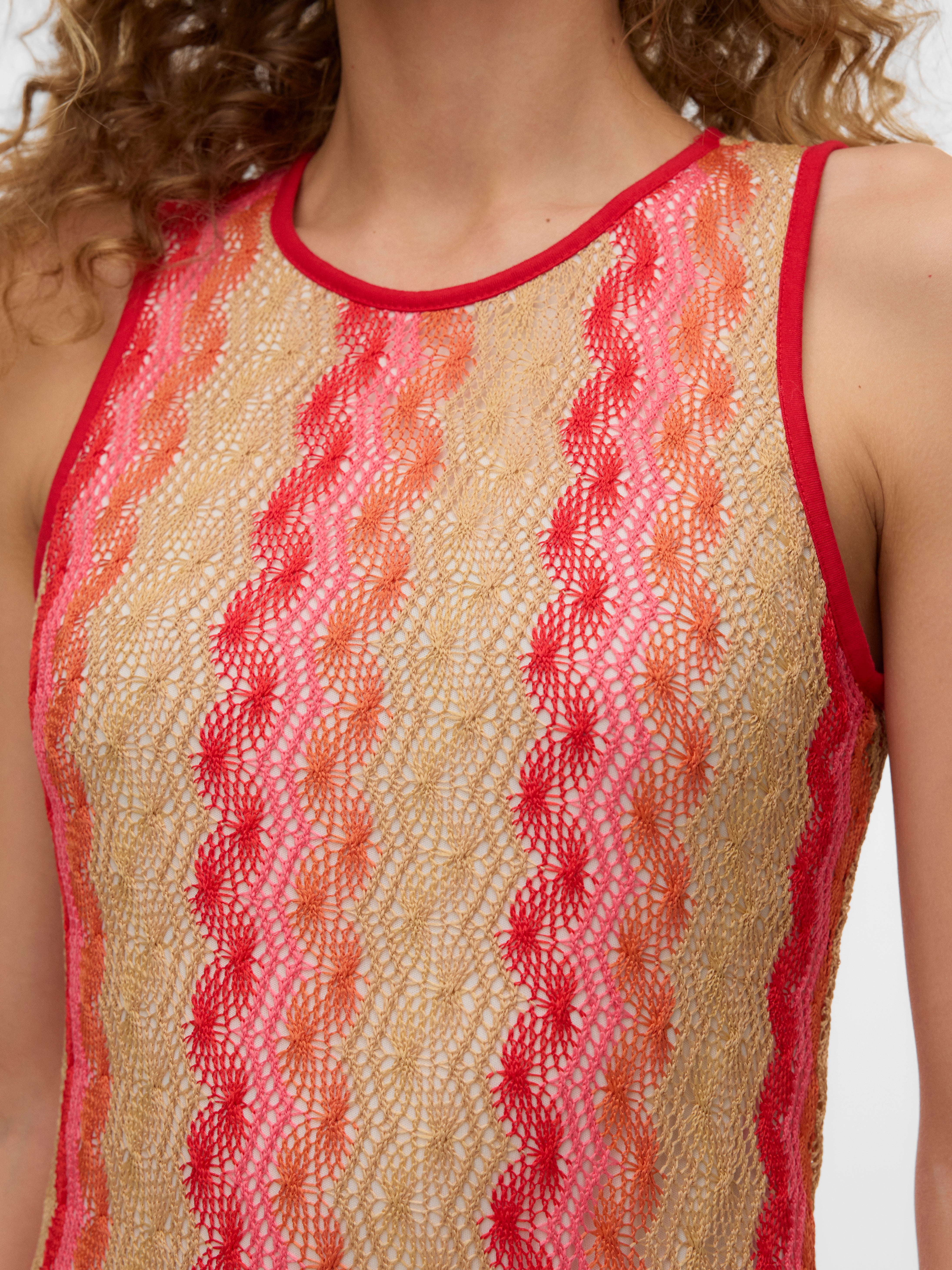 Close-up of sleeveless top with red, pink, and beige lace pattern and red trim around neck and armholes