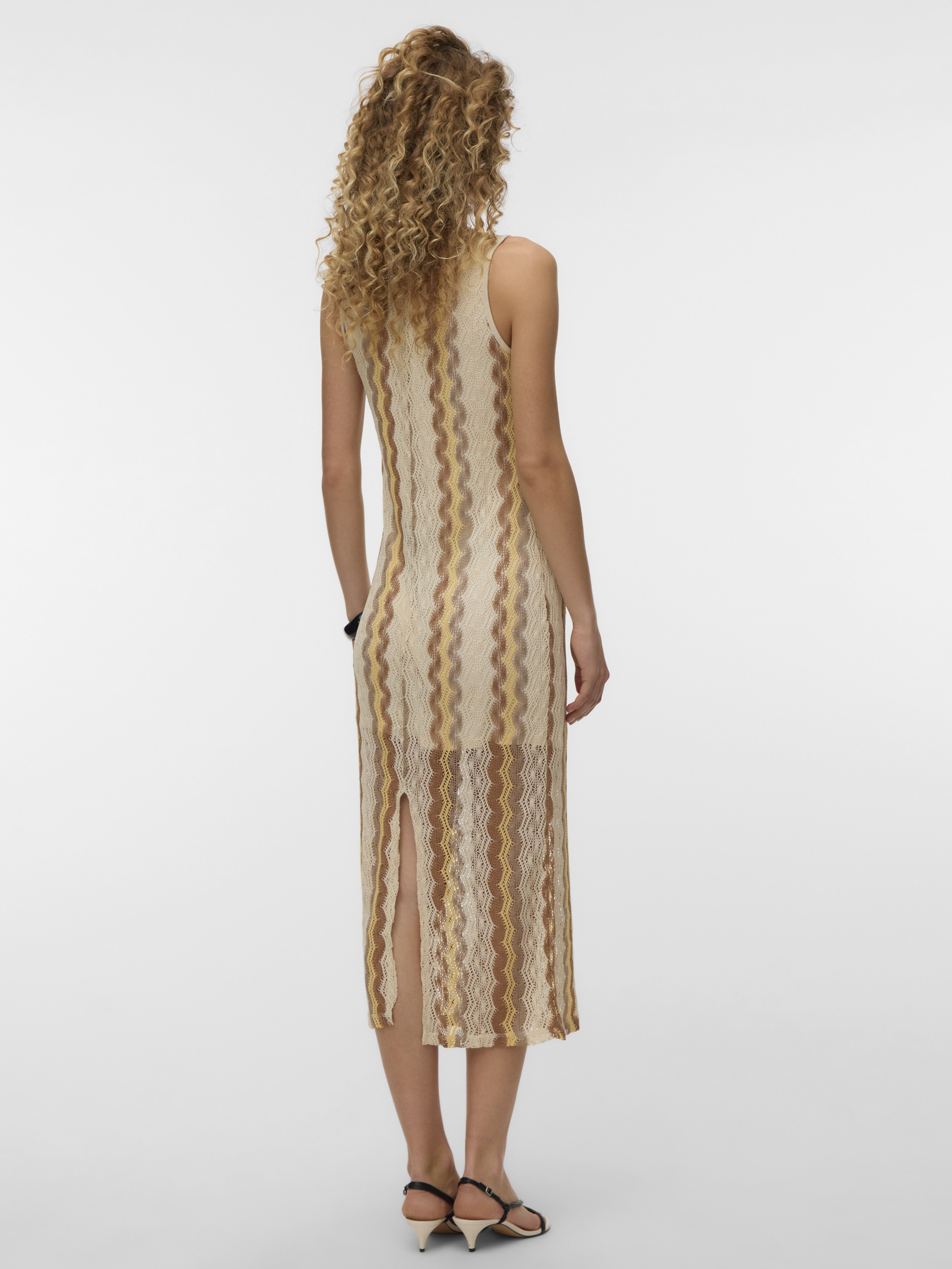 Sleeveless midi dress with vertical wavy stripes in beige and brown tones and a back slit, paired with black sandals.