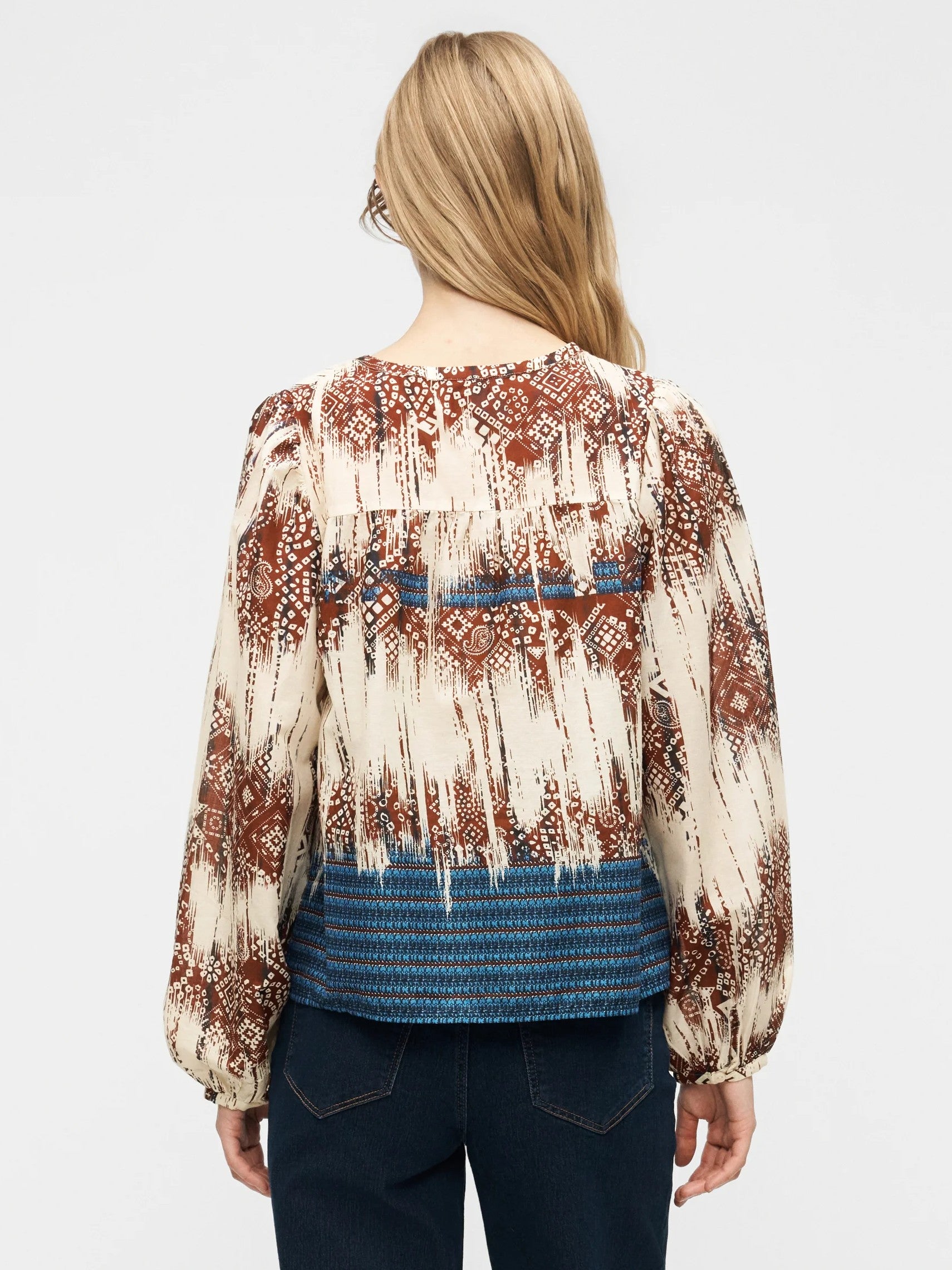 Back view of a long-sleeve patterned top with rust, cream, and blue colors paired with dark denim jeans.