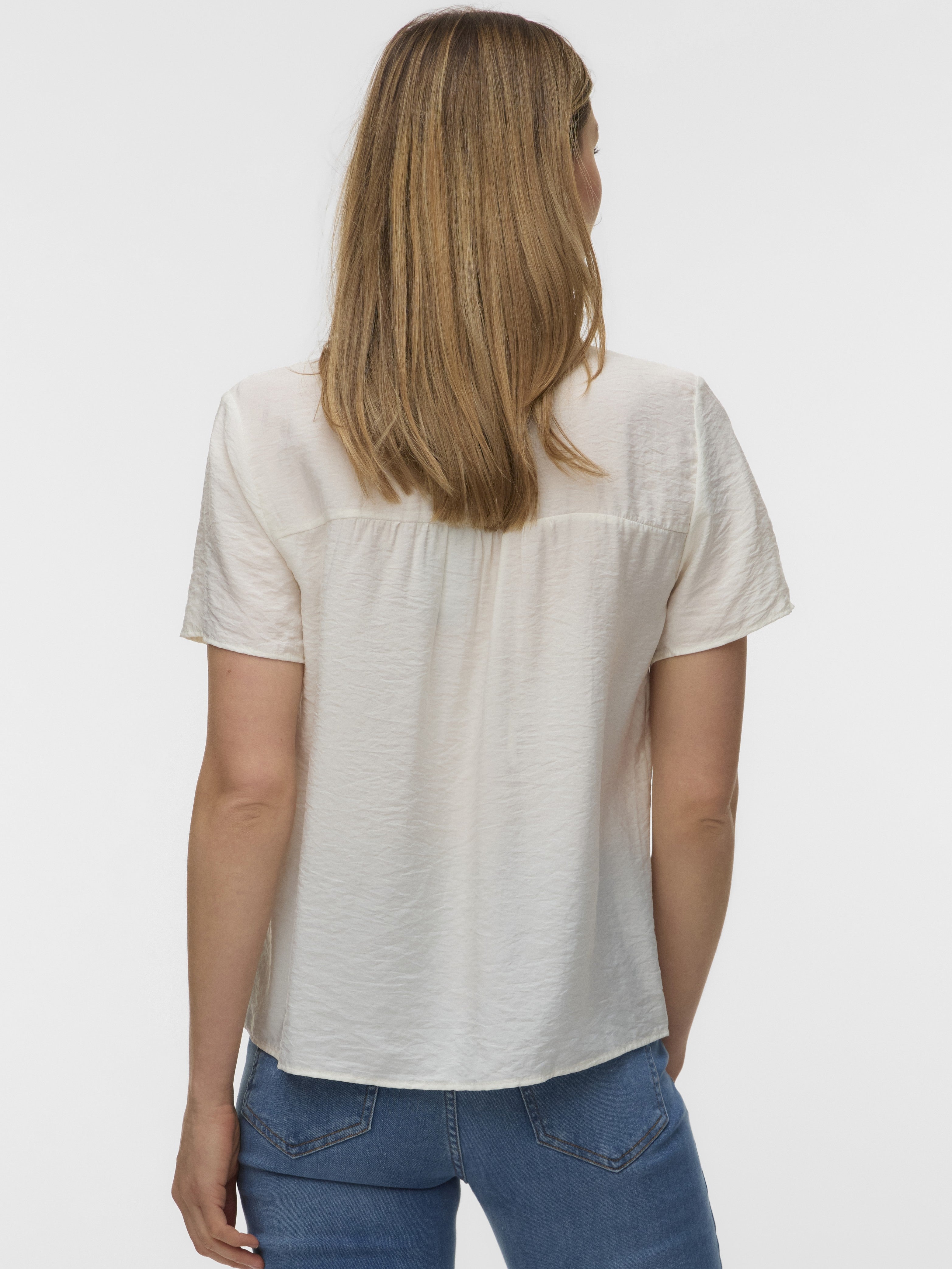 Back view of a cream short-sleeve textured top paired with blue denim jeans on a neutral background.