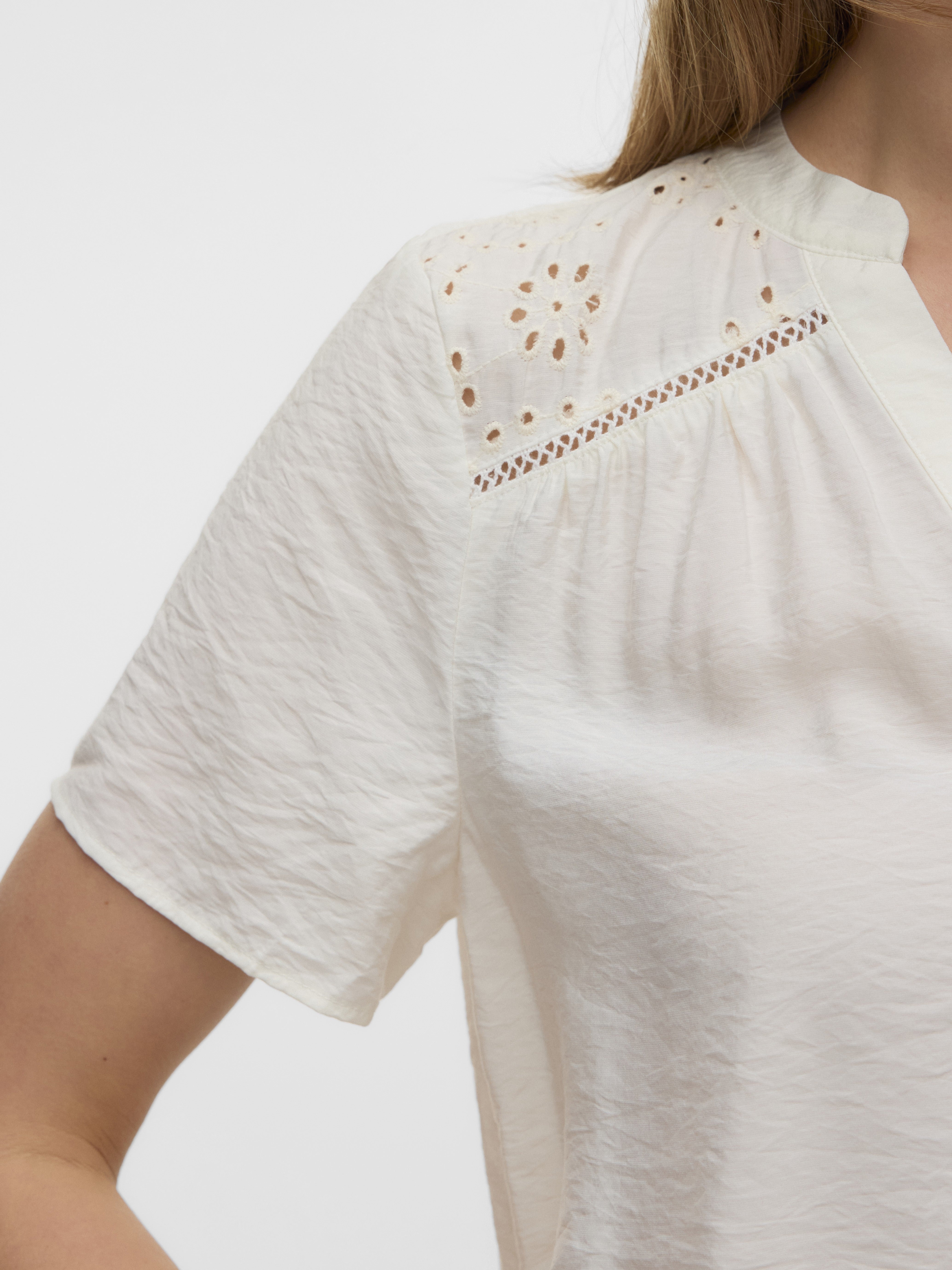 Close-up of a white textured short-sleeve top with delicate eyelet detailing on the shoulder and upper chest area