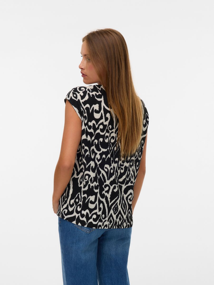 Back view of a person wearing a sleeveless black and beige abstract patterned top with blue denim jeans.