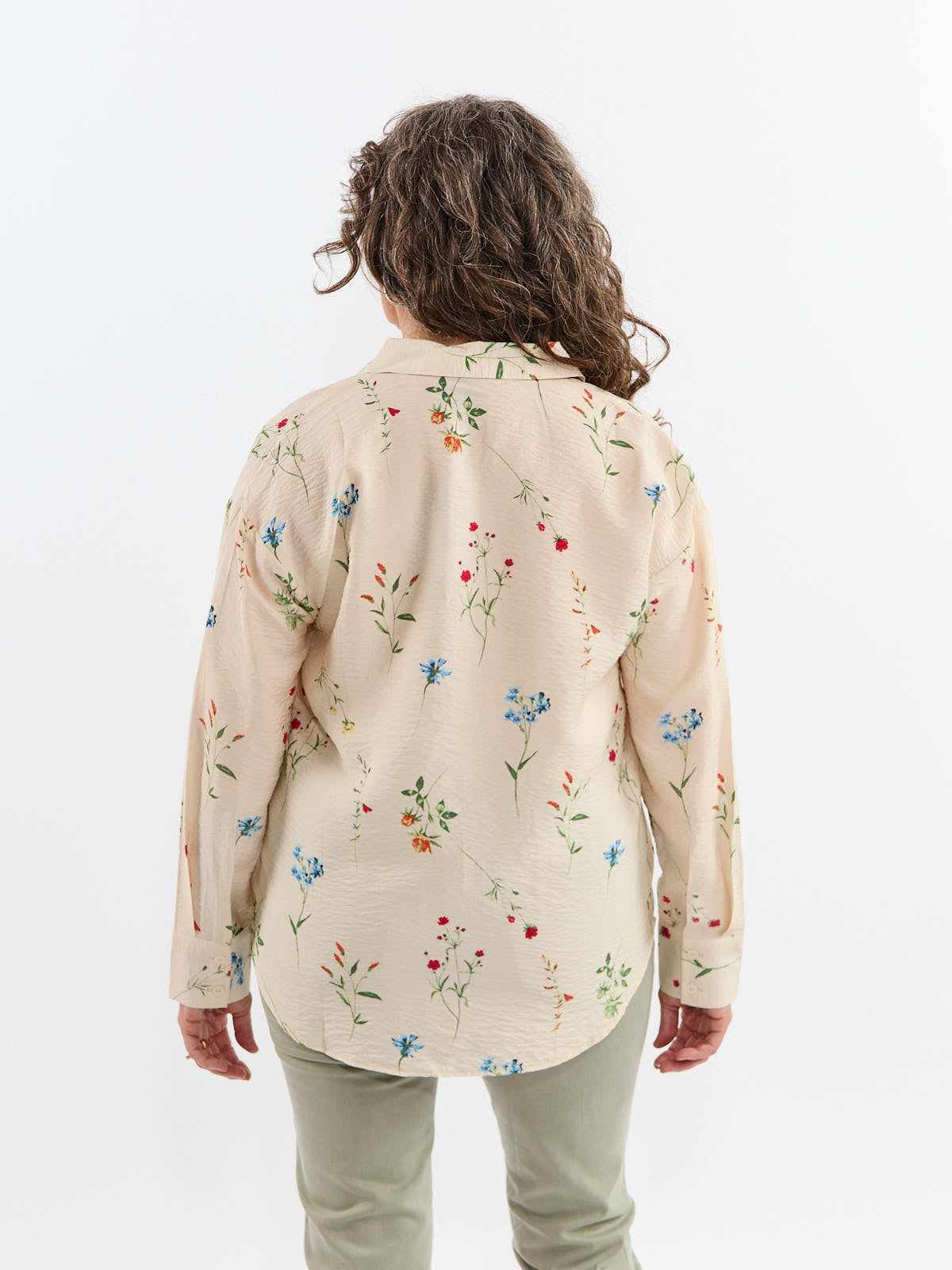 Back view of a person wearing a beige long-sleeve shirt with a multicolored floral print and light-colored pants.