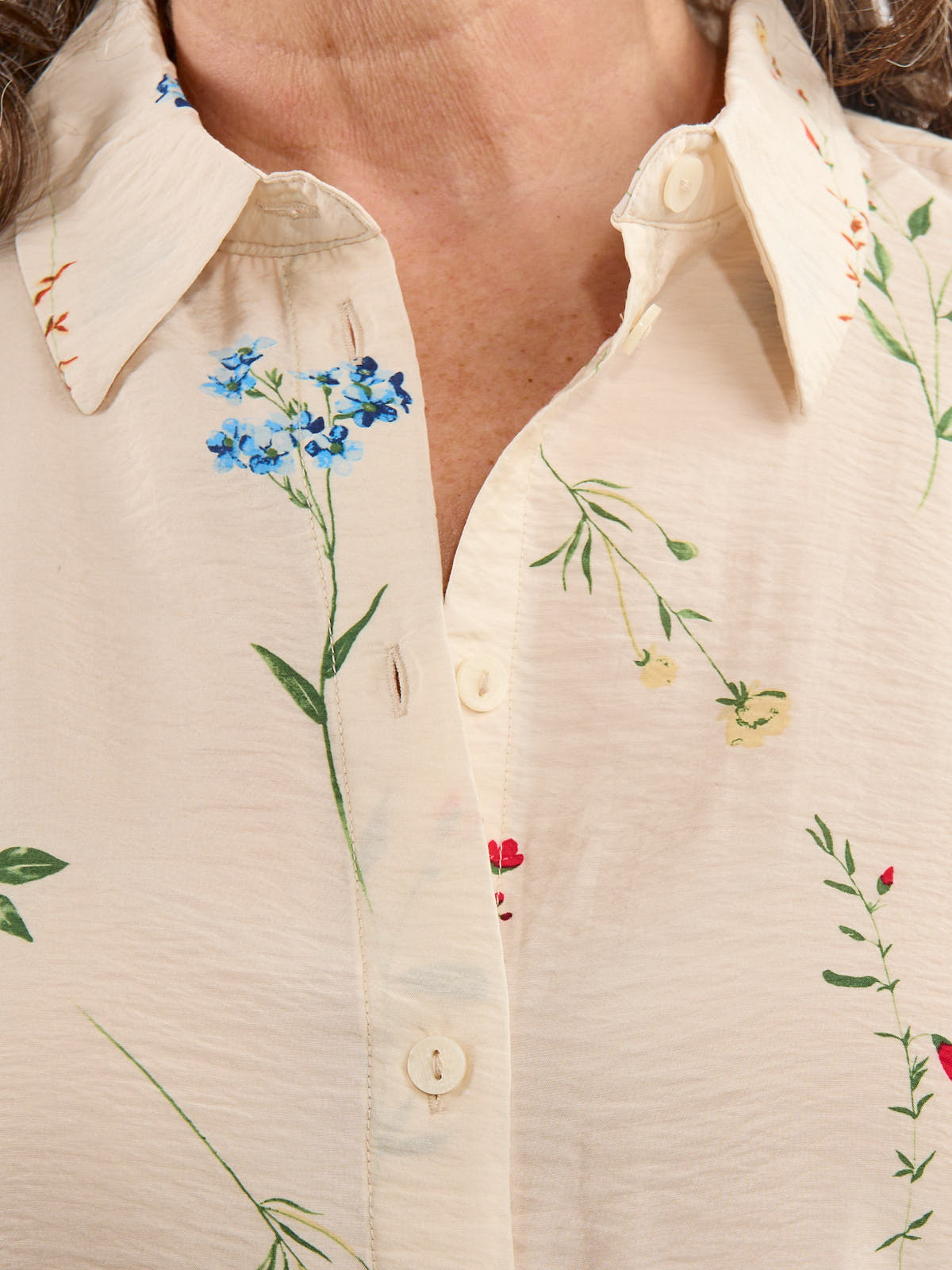 Close-up of beige button-up shirt with embroidered colorful floral designs on collar and front panel