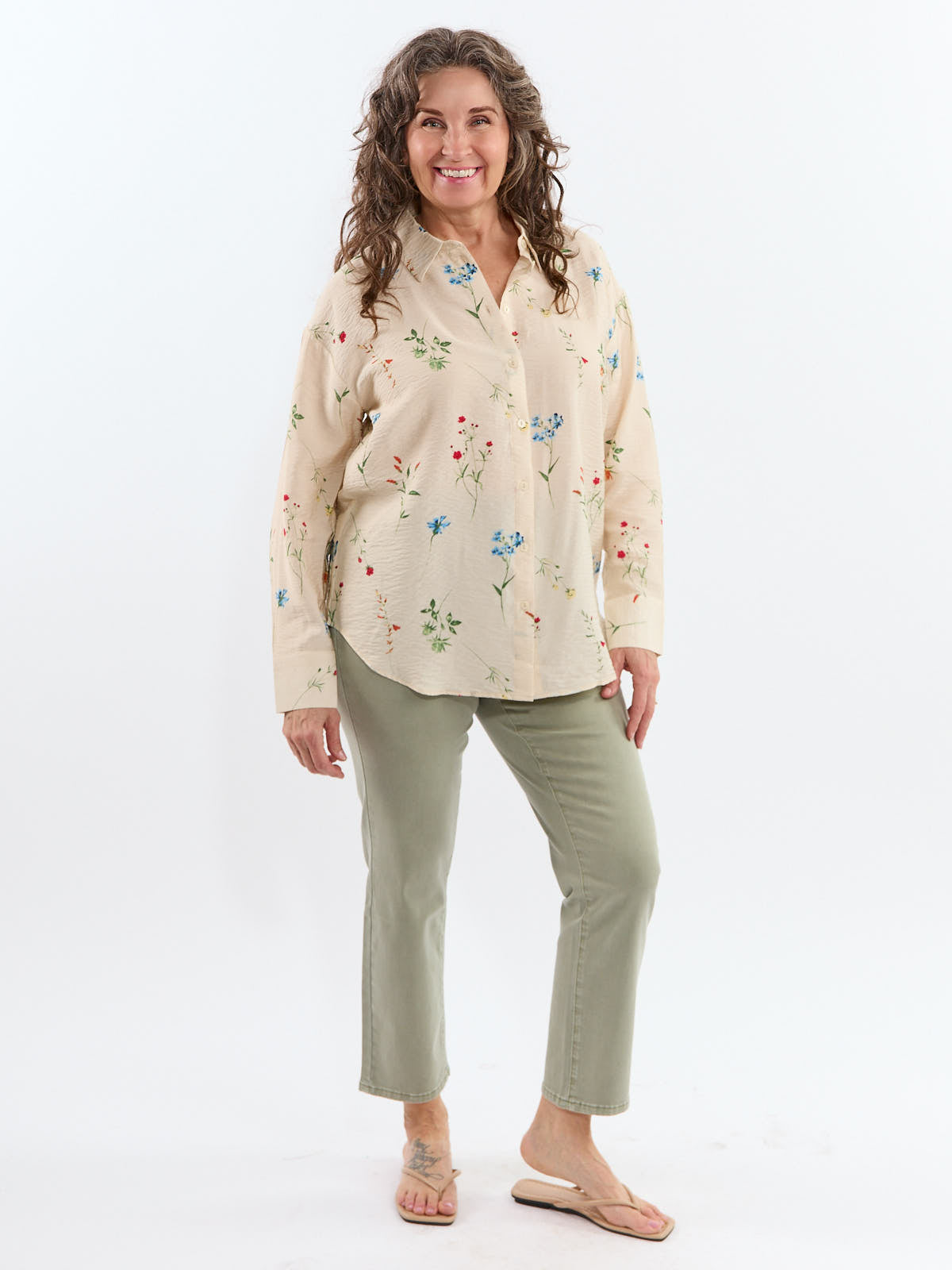 Smiling person in a beige floral long-sleeve top paired with light green pants and beige sandals.